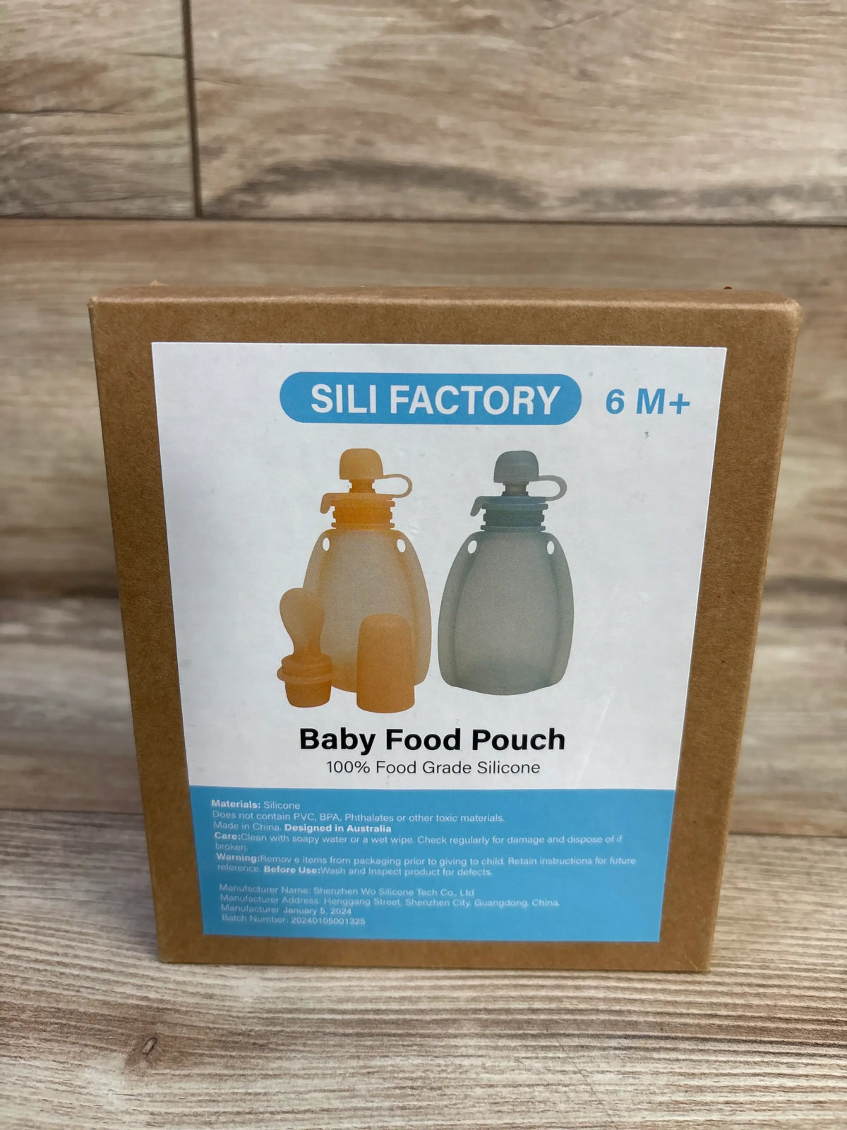 Front view of Sili Factory 2-pack reusable baby food pouch package marked for ages 6 months and up, showing two silicone pouches and spoons on a wood surface