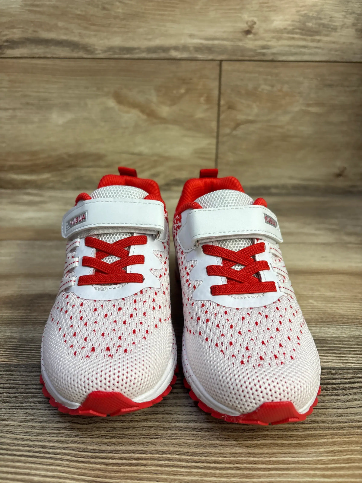 Front view of Kubua toddler running sneakers, size 12C, white mesh with red laces, Velcro strap and red sole on wood floor