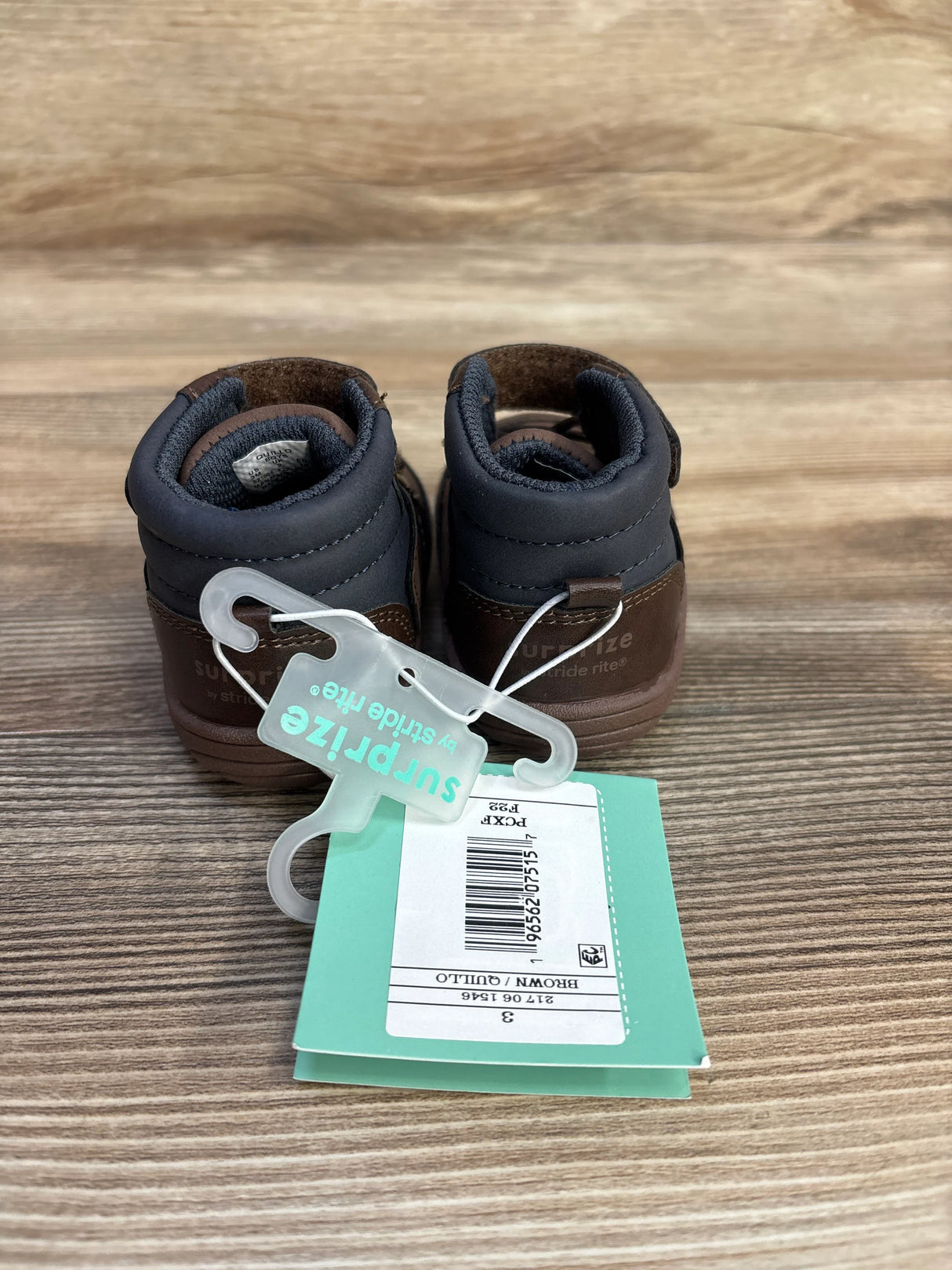 Pair of brown and black Stride Rite Surprize kids shoes with teal tag on wood surface
