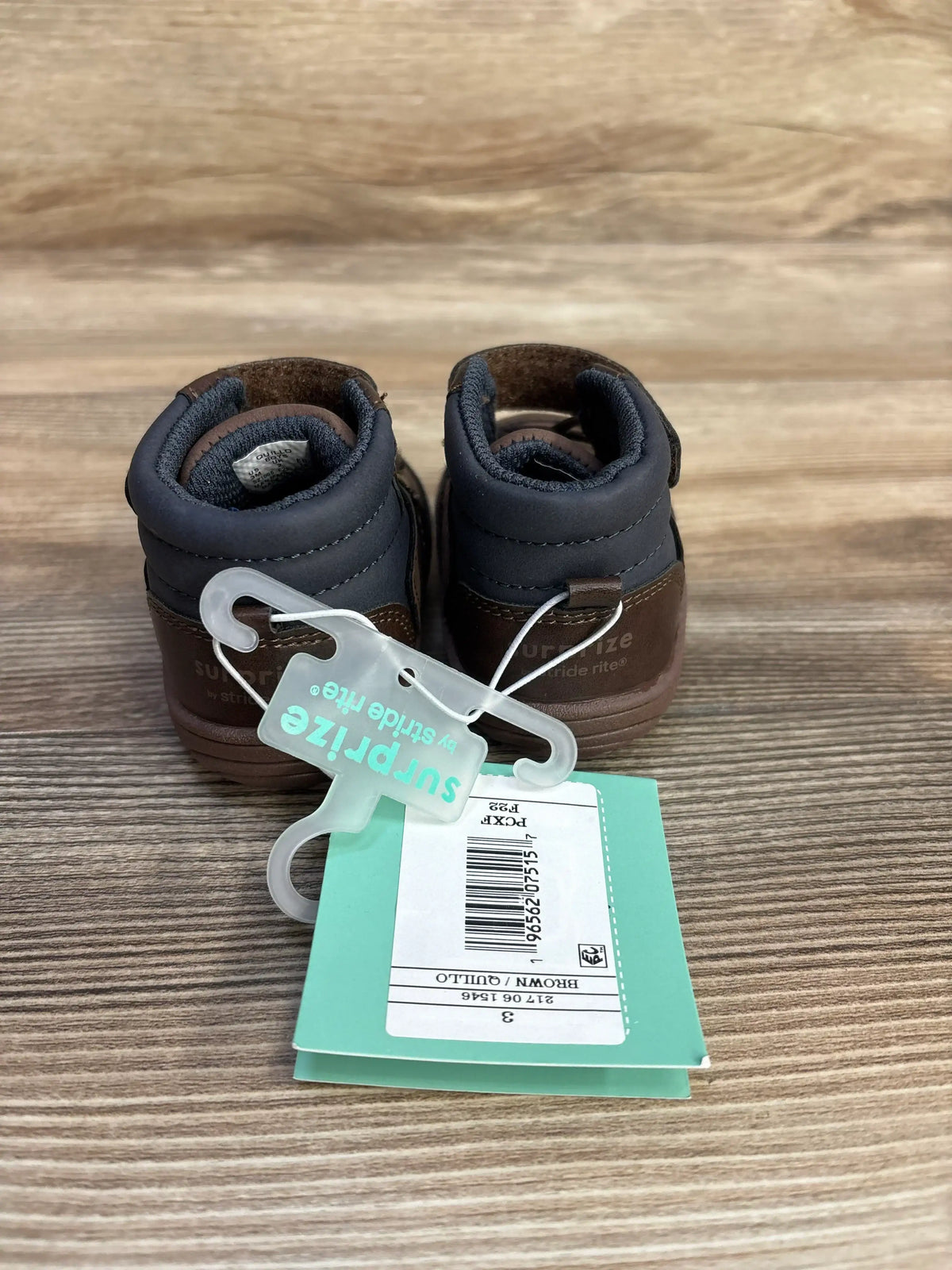 Pair of brown and black Stride Rite Surprize kids shoes with teal tag on wood surface