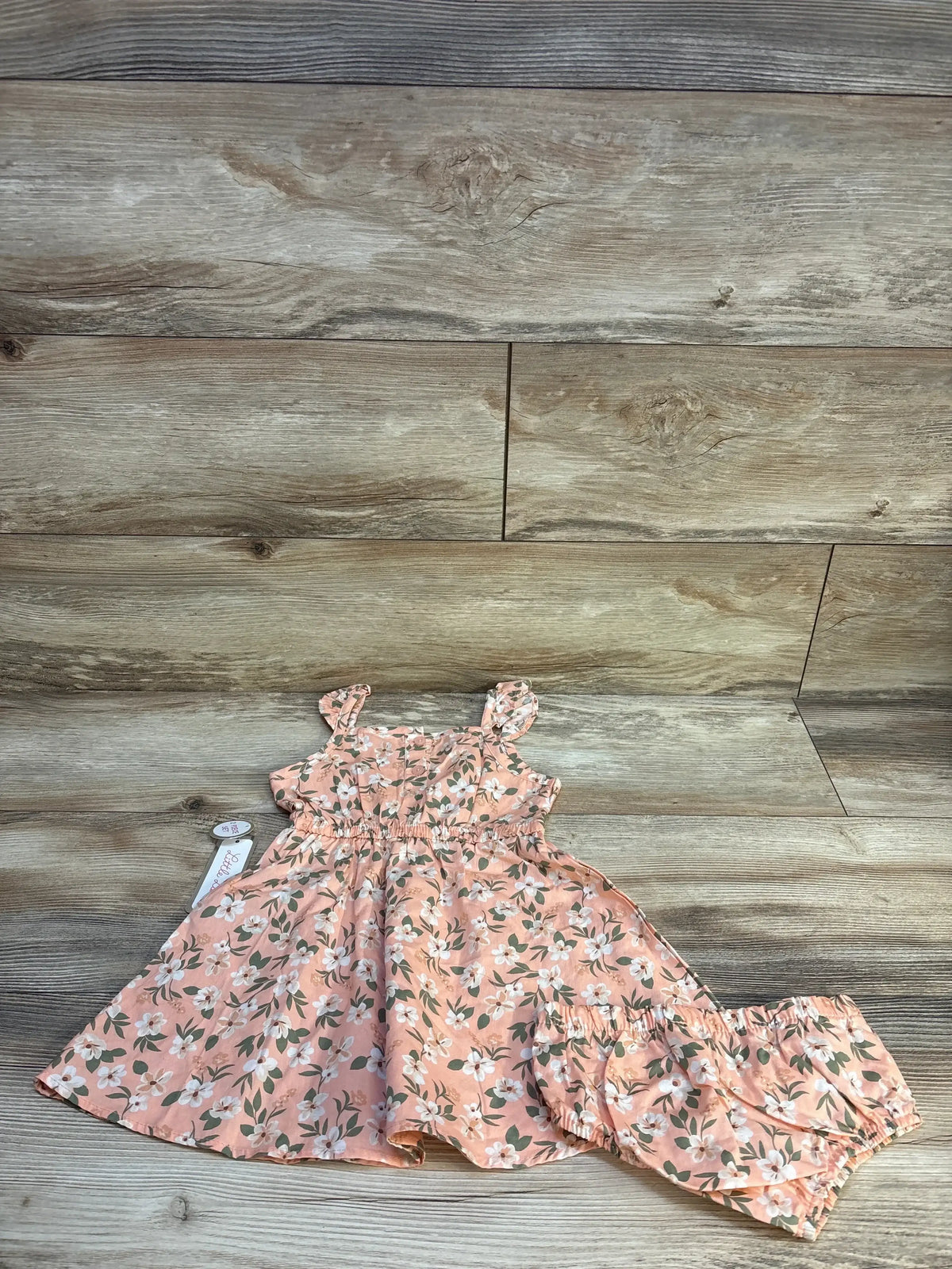 Peach floral baby dress and matching bloomers set displayed on wooden background