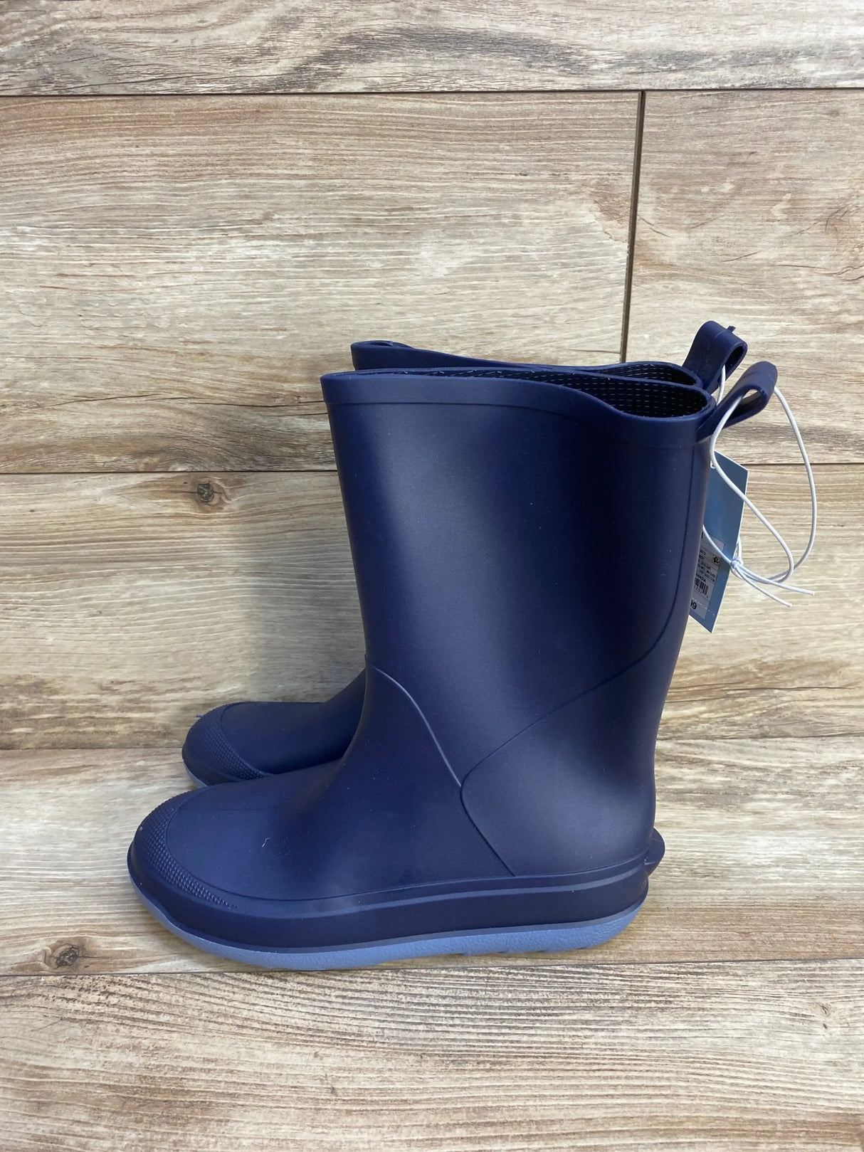 Side view of Cat and Jack Andy navy toddler slip-on rain boots showing pull loops and textured gray sole on wooden floor background
