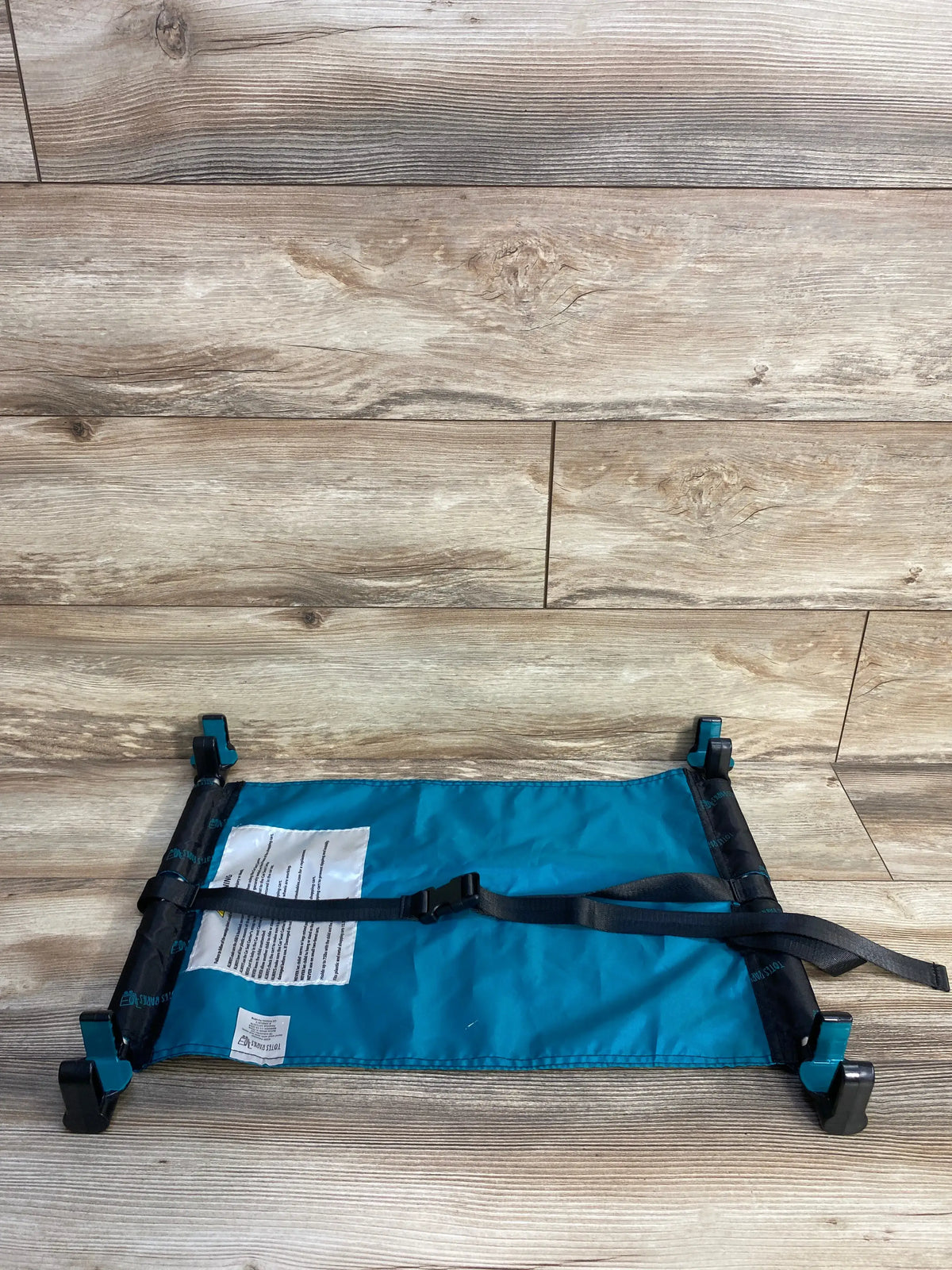 Top-down view of Totes Babies cart and car seat hammock with teal fabric, center buckle, adjustable straps on wood background