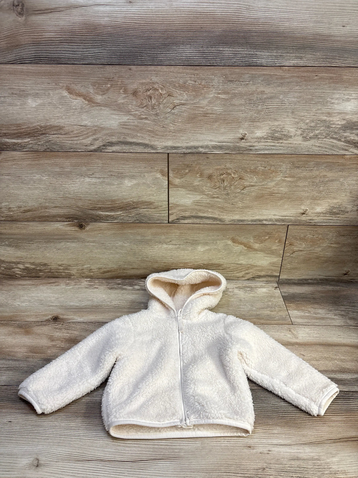 Flat lay of cream toddler teddy fleece jacket with hood and front zipper on wood background, size 12 to 18 months