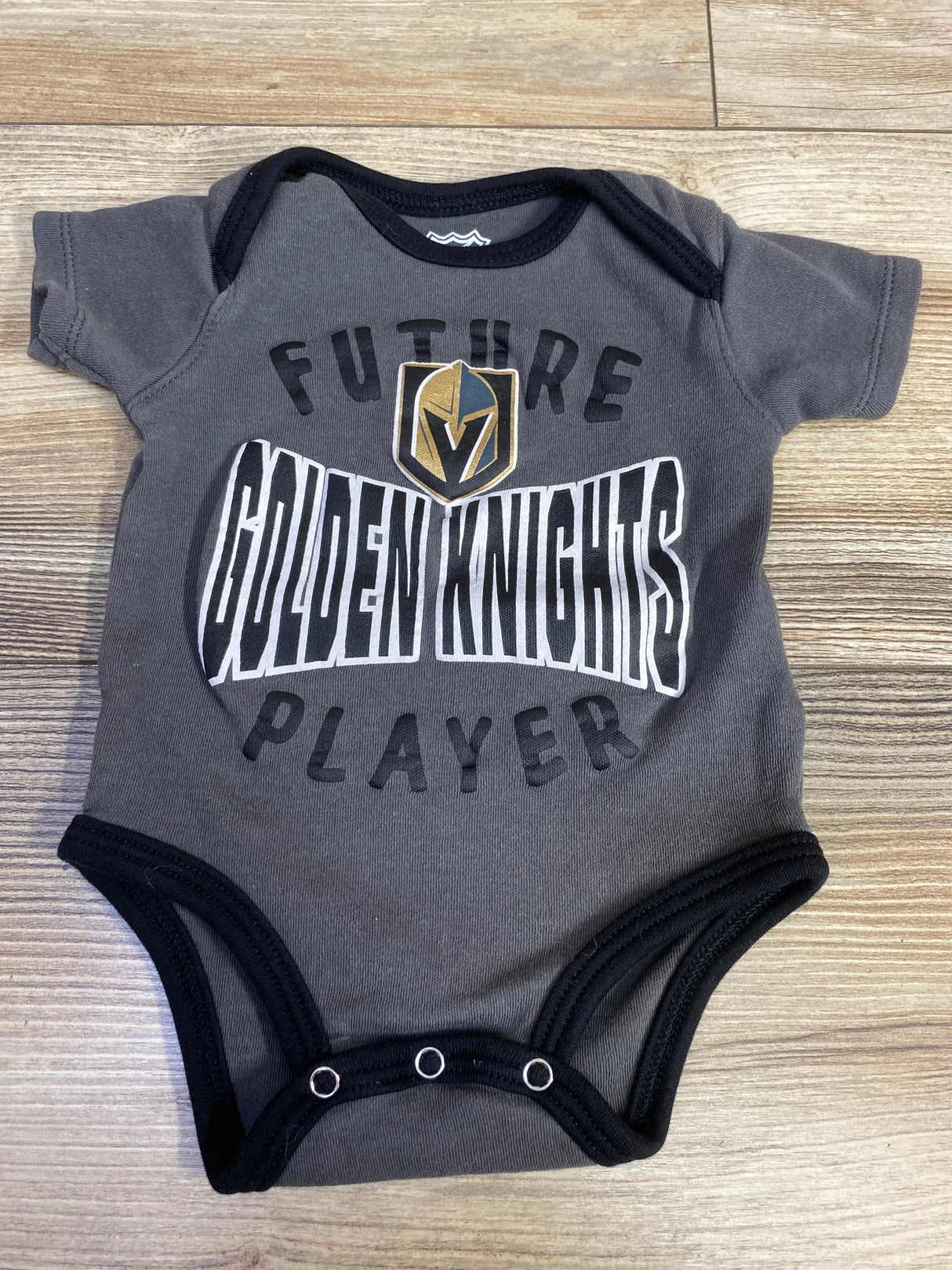 Gray Vegas Golden Knights baby onesie with 'Future Golden Knights Player' text on wood floor