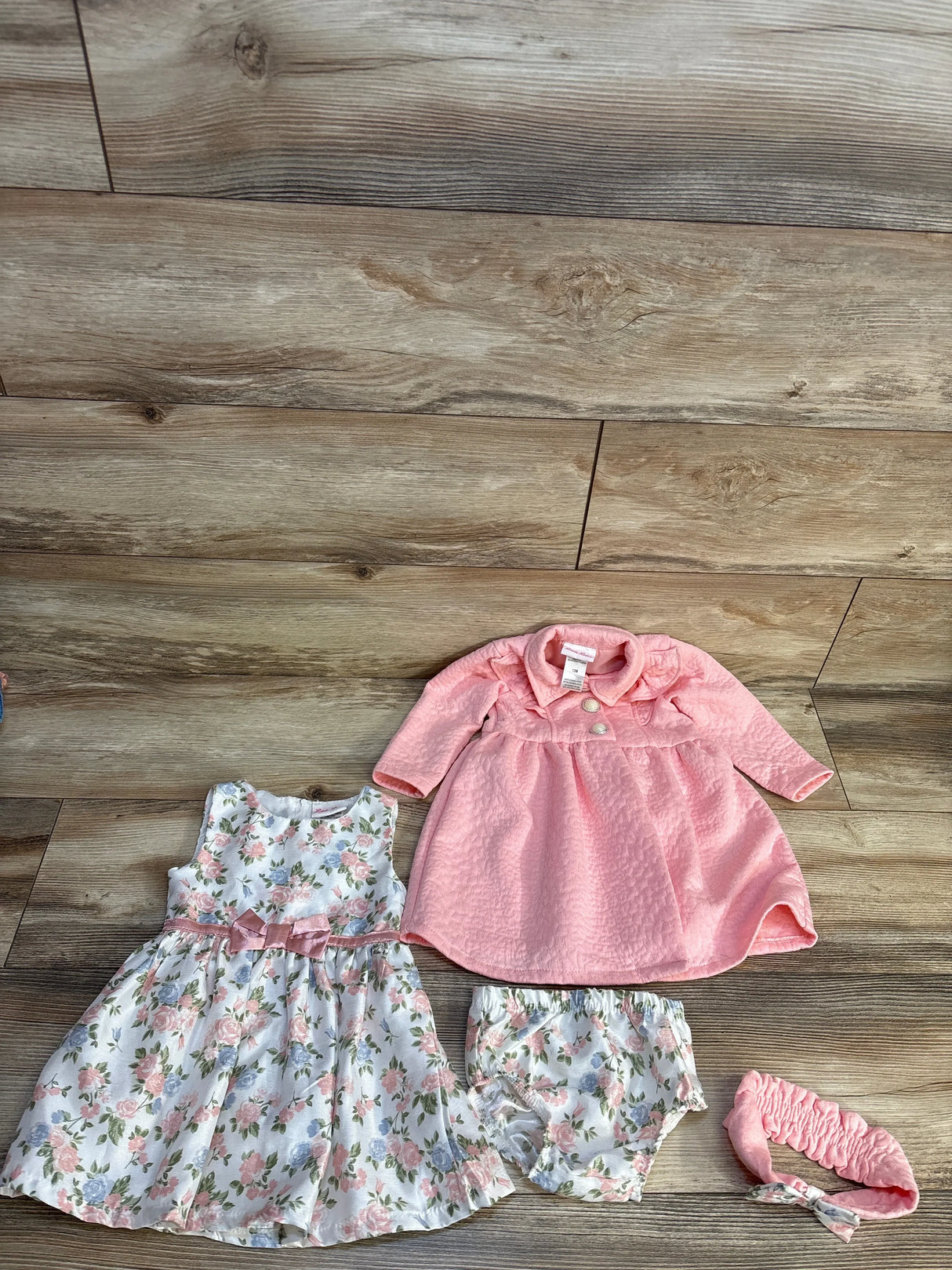 Pink floral baby dress set with matching bloomers and headband on wood floor