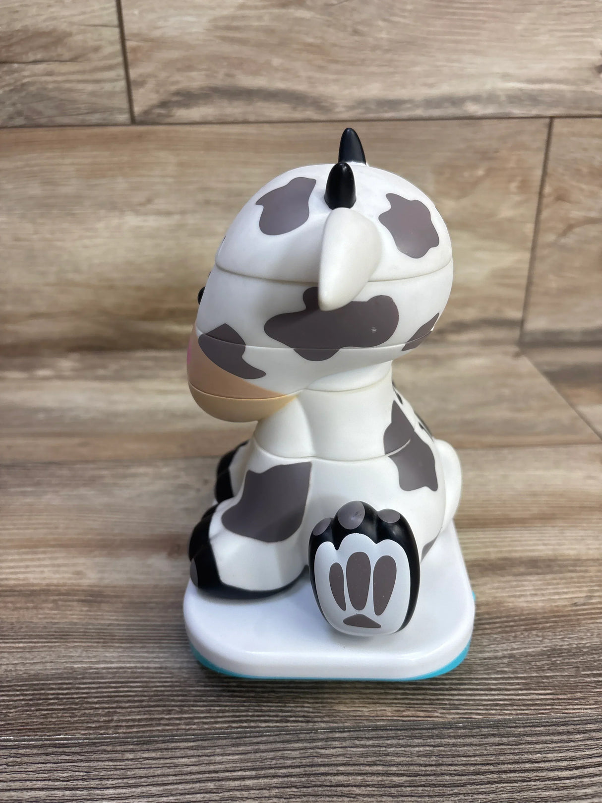 Side view of Stack-a-Roos baby cow stacking toy showing stacked removable sections, gray cow spots and paw base on wood table