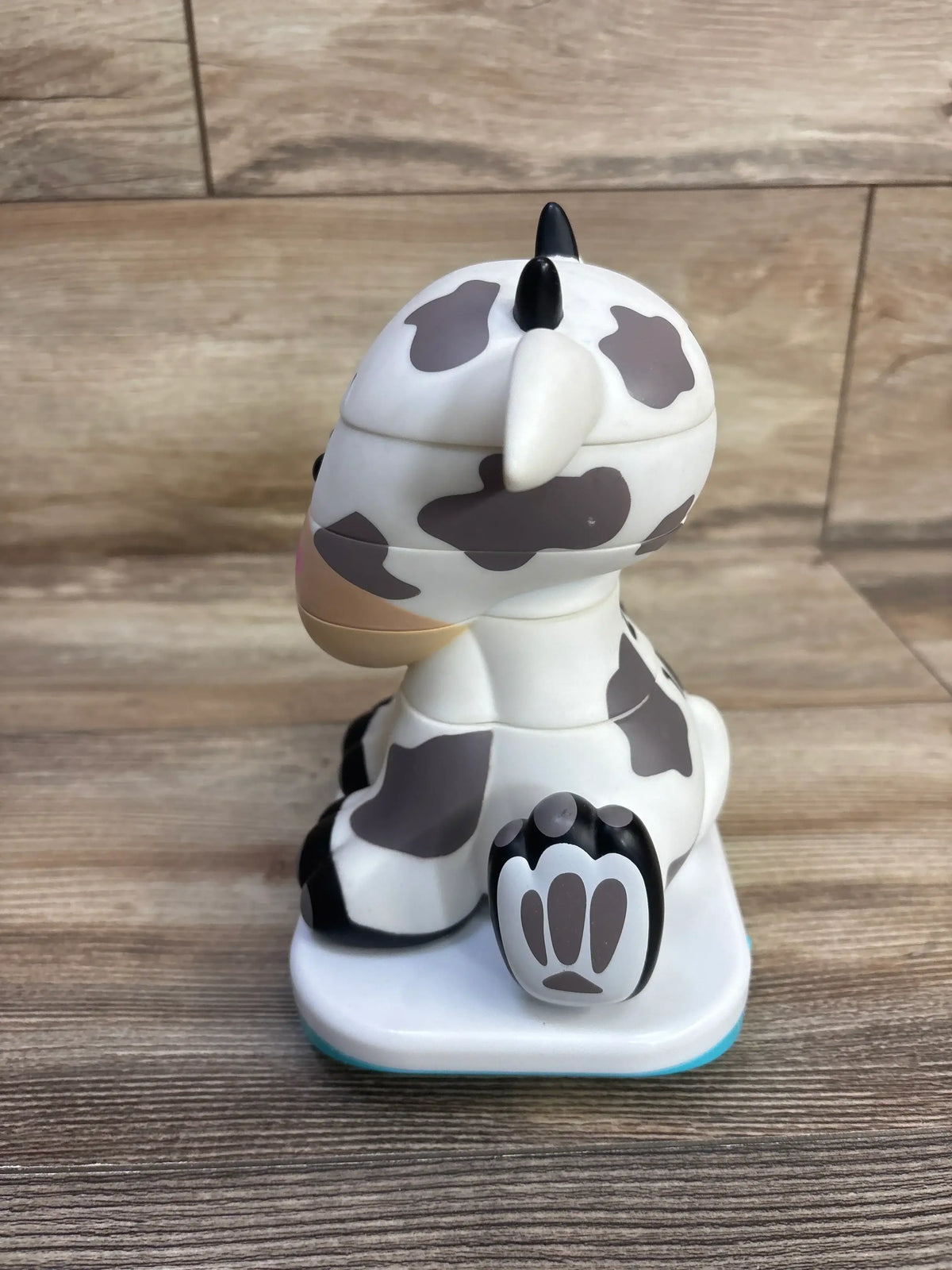 Side view of Stack-a-Roos baby cow stacking toy showing stacked removable sections, gray cow spots and paw base on wood table