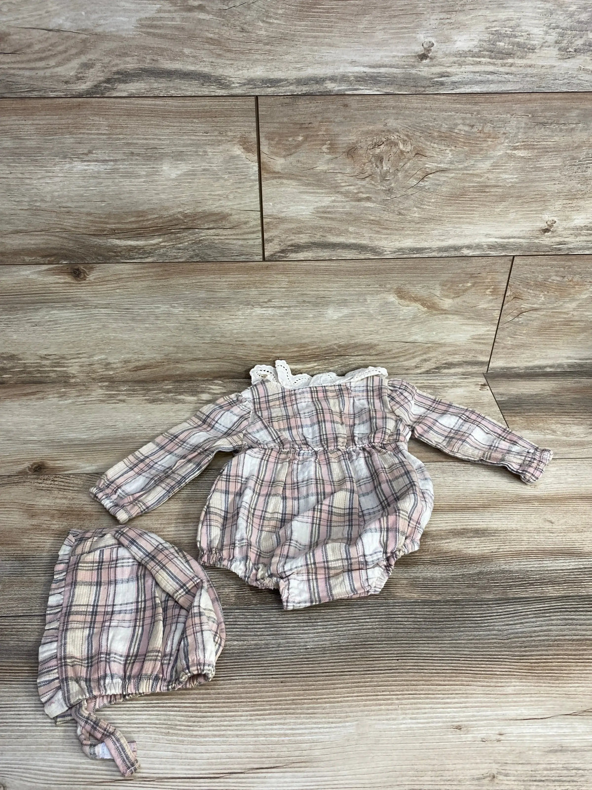 Flat-lay of Nicole Miller pink and white plaid bubble romper and matching bonnet showing lace-trim collar and long sleeves on wood background