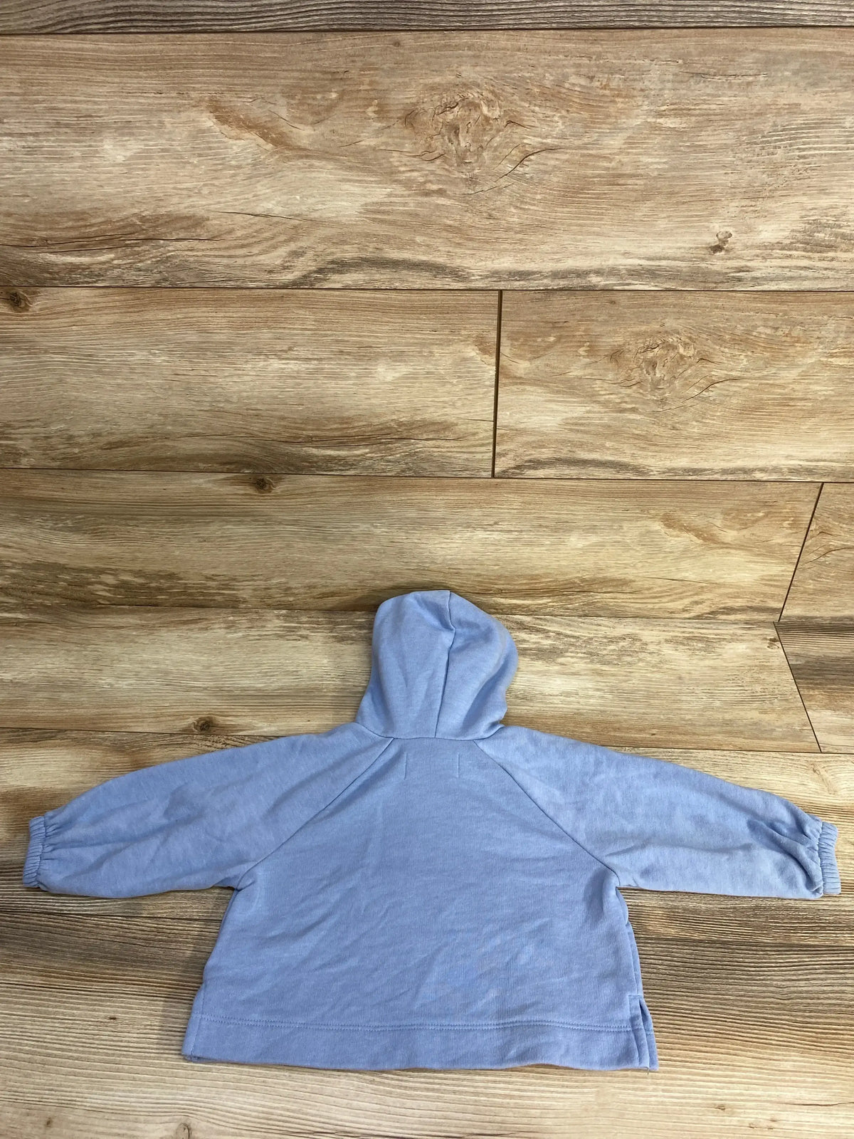 Light blue hooded sweatshirt laid flat on wooden floor with long sleeves and elastic cuffs