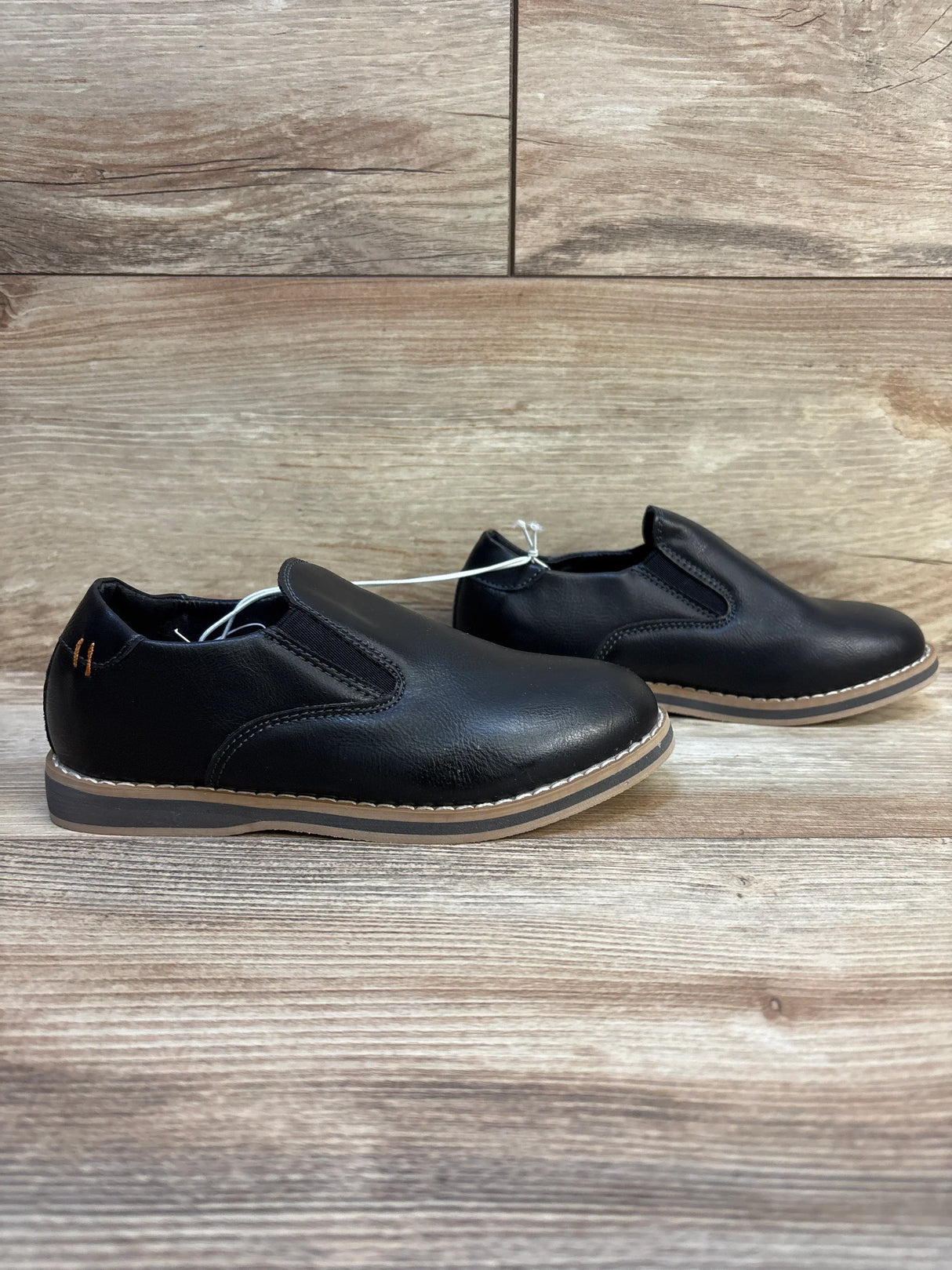 Black slip-on kids dress shoes with rubber soles on wood background, children's footwear