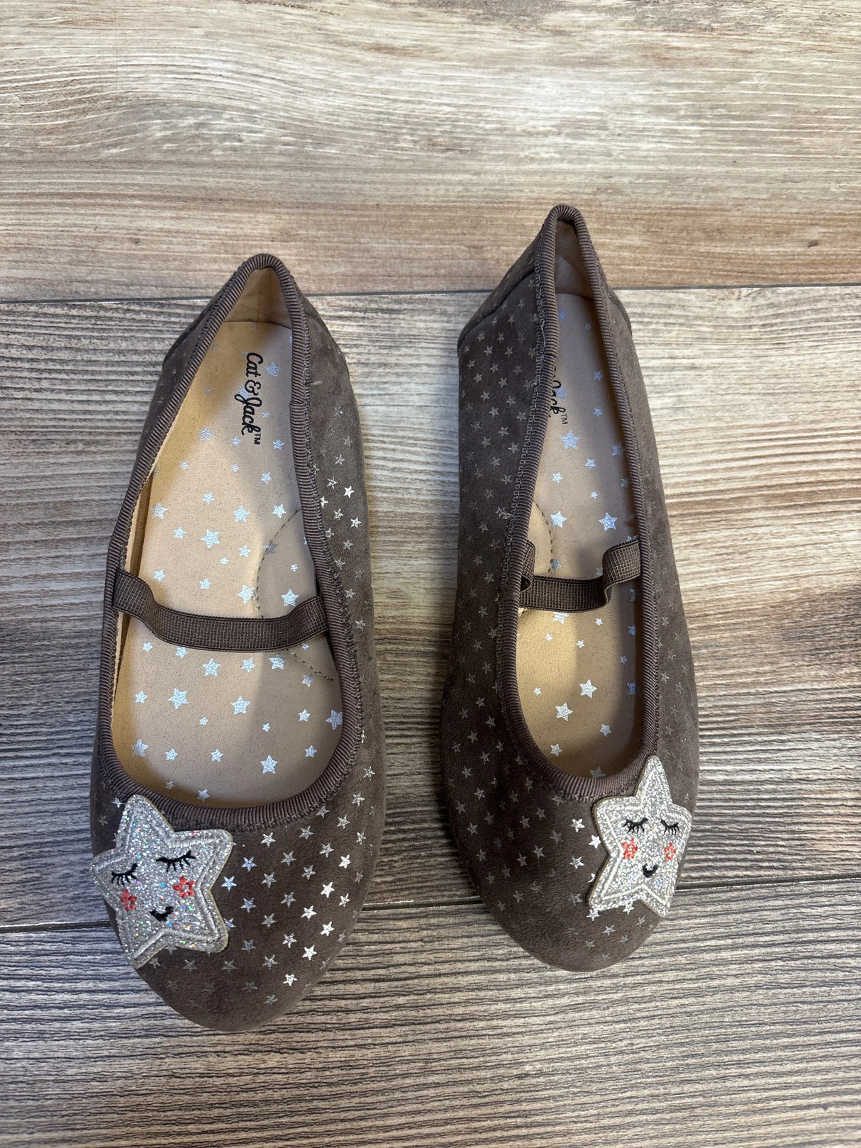 Brown girls' Mary Jane shoes with silver star patterns and star patches on wooden floor