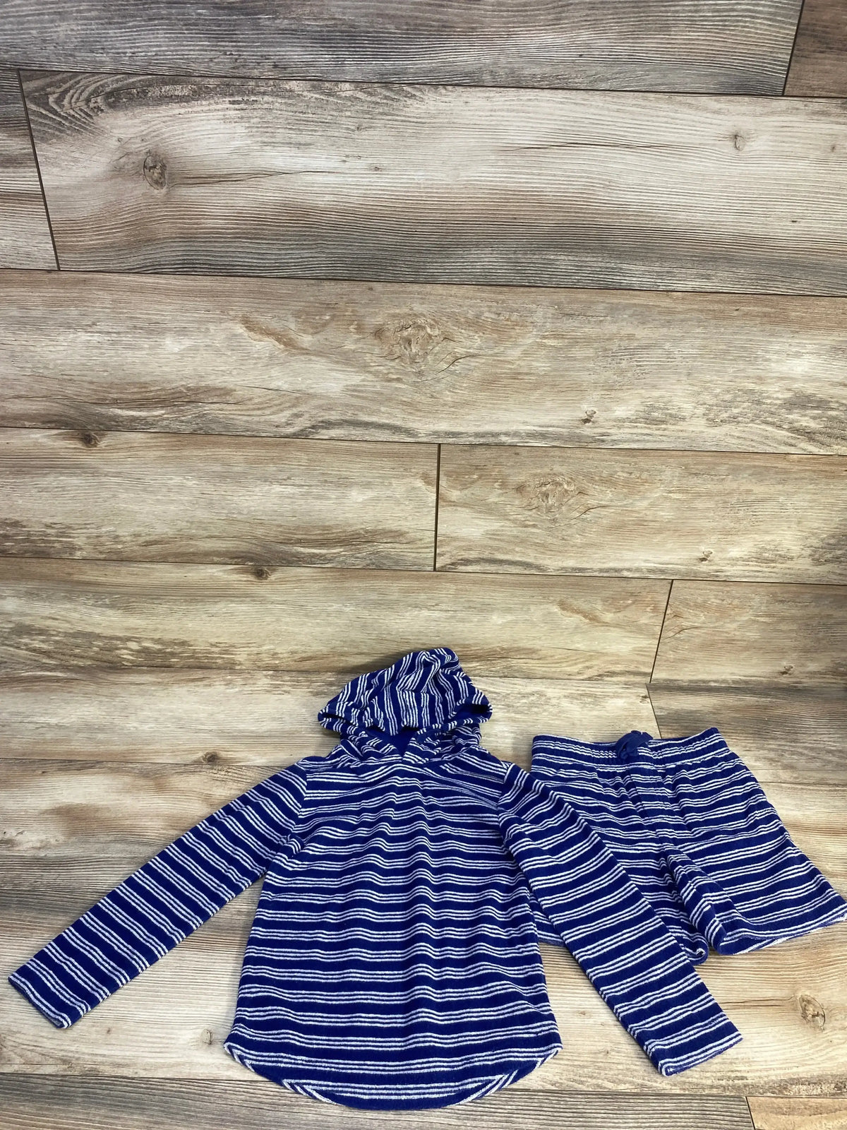 Flat lay of navy terry hoodie and matching shorts showcasing white horizontal stripes and hood on light wood floor background