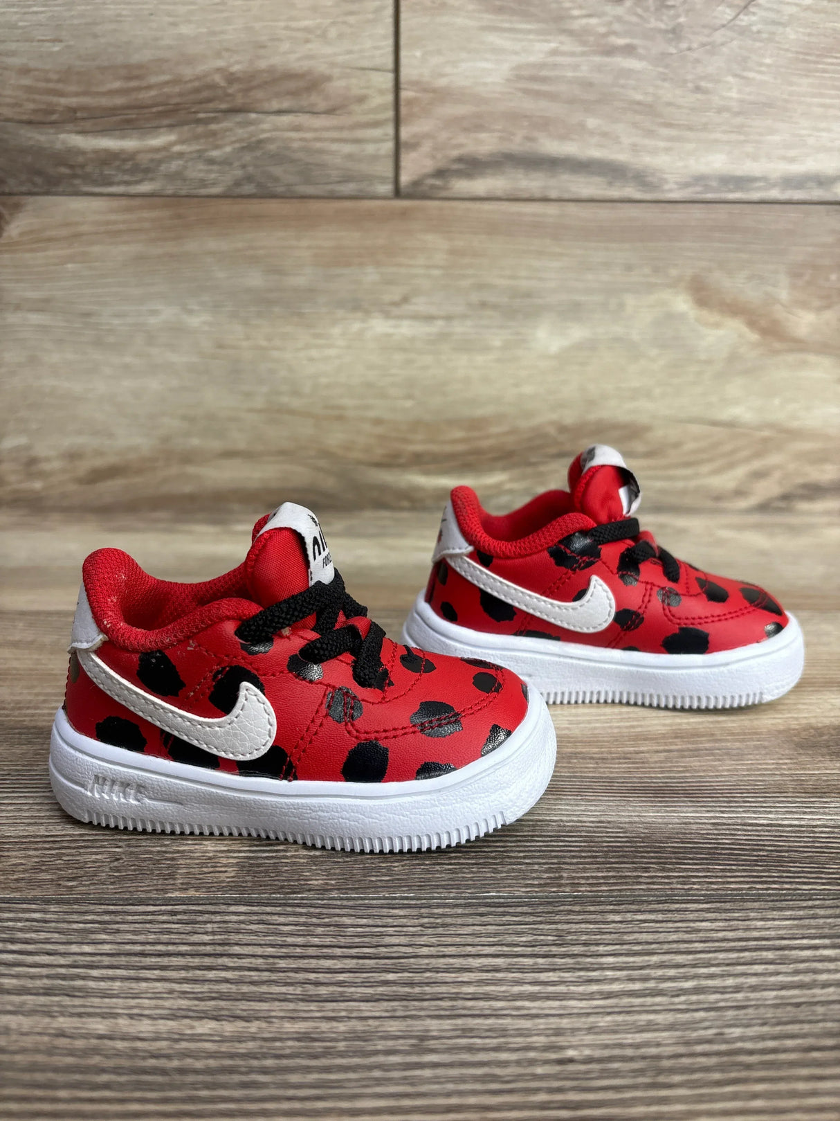 Red and black polka dot toddler sneakers with white Nike swoosh and white soles on wooden surface