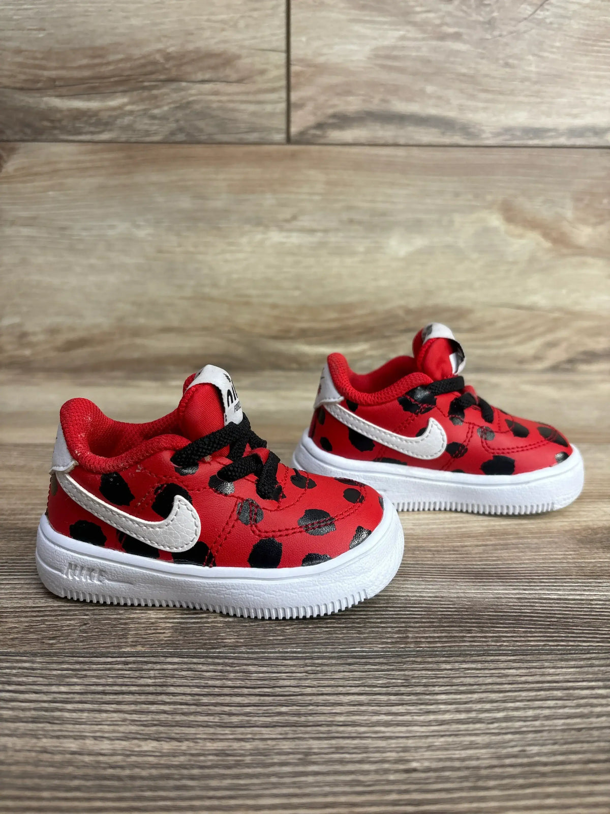 Red and black polka dot toddler sneakers with white Nike swoosh and white soles on wooden surface