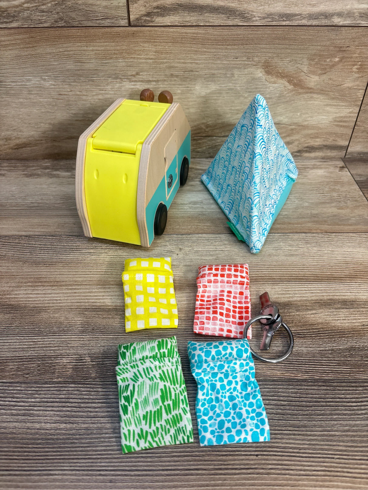Colorful wooden toy van with patterned fabric pouches and keychain on wood floor