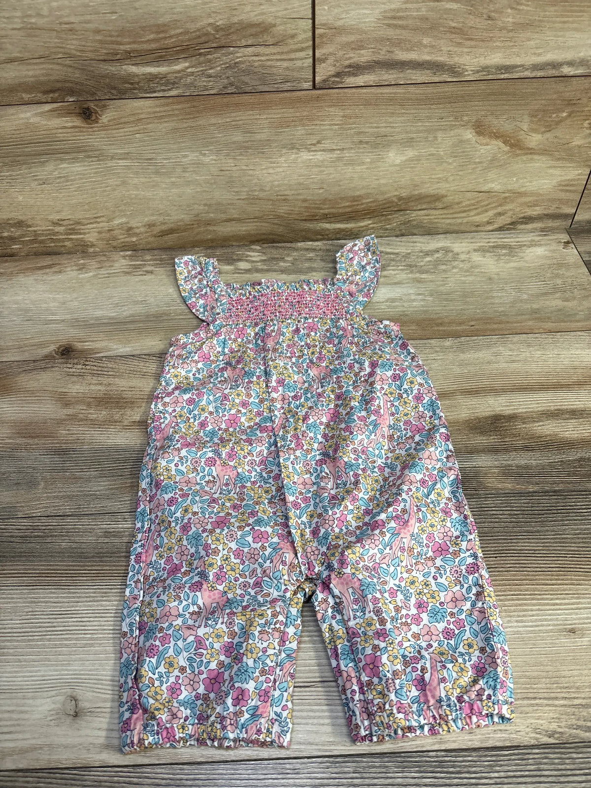 Flat lay of smocked floral sleeveless jumpsuit with ruffle straps and elastic ankles on wooden background, size 6-12 months