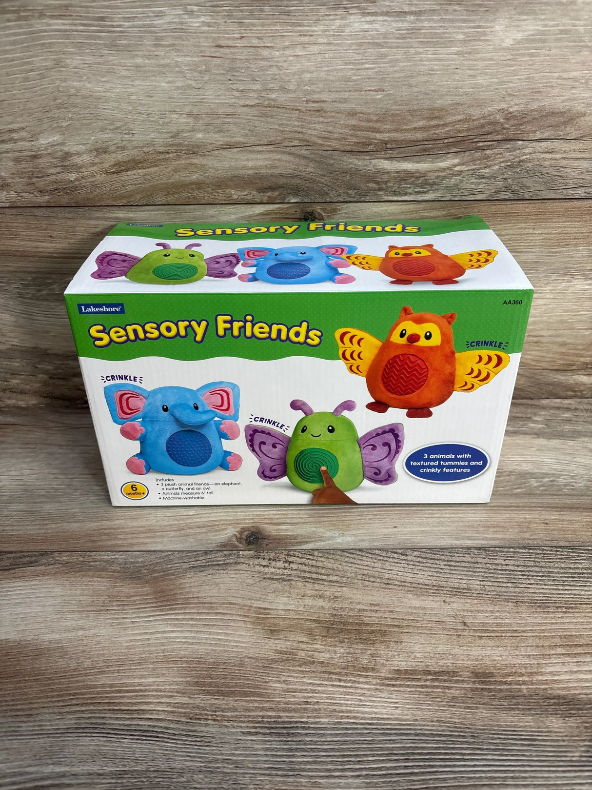 Front view of Lakeshore Sensory Friends boxed set showcasing three plush toys (blue elephant, green bug, orange owl) with textured tummies and crinkly features on a wood tabletop