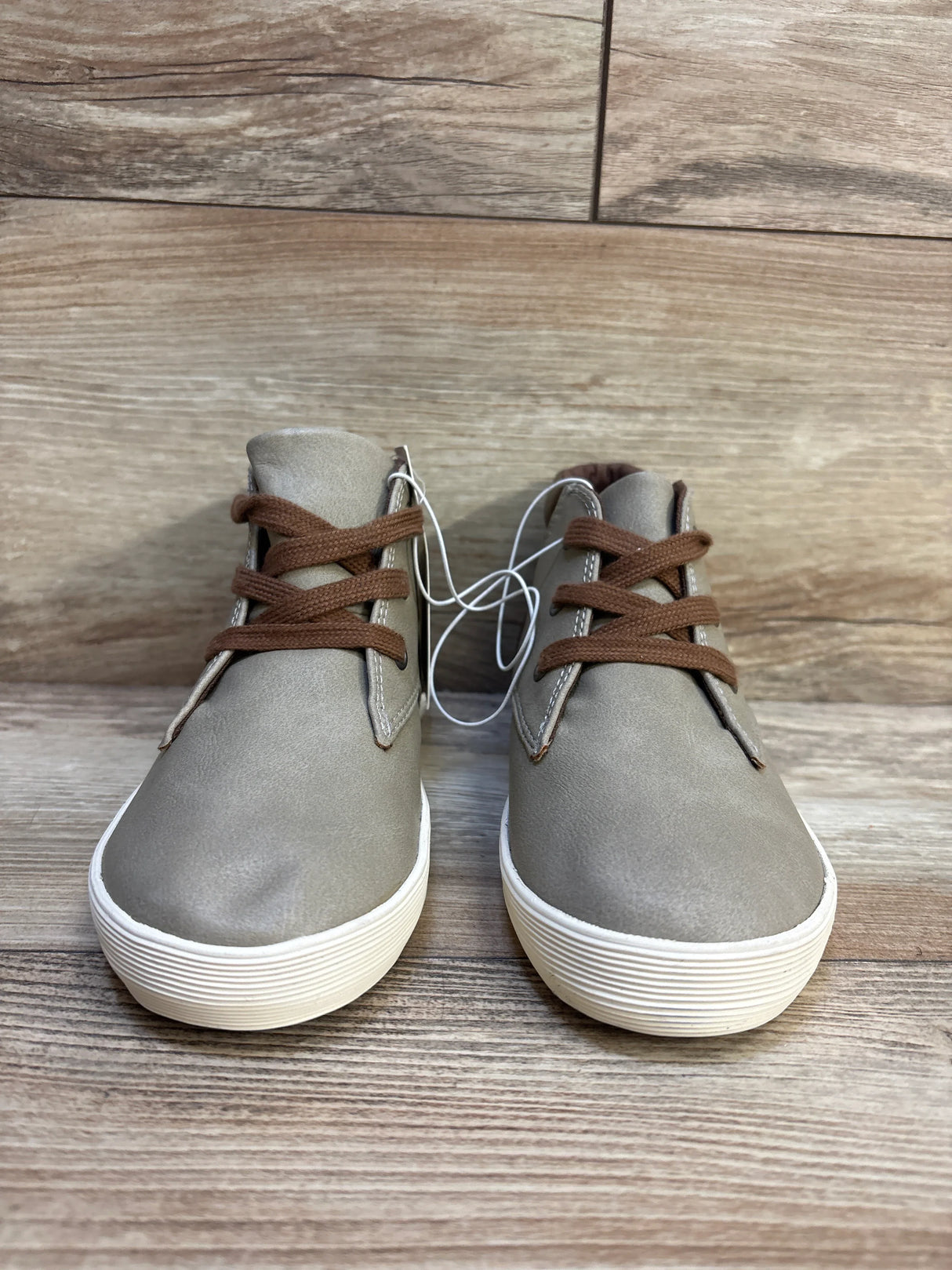 Kids taupe faux leather sneakers with brown laces and white soles on wood floor