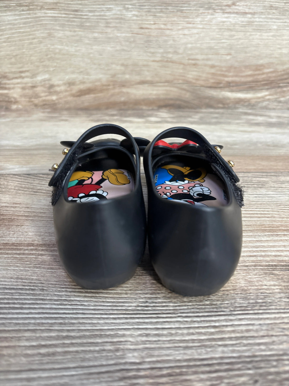 Black children's Mary Jane shoes with Minnie and Mickey Mouse insoles on a wooden surface