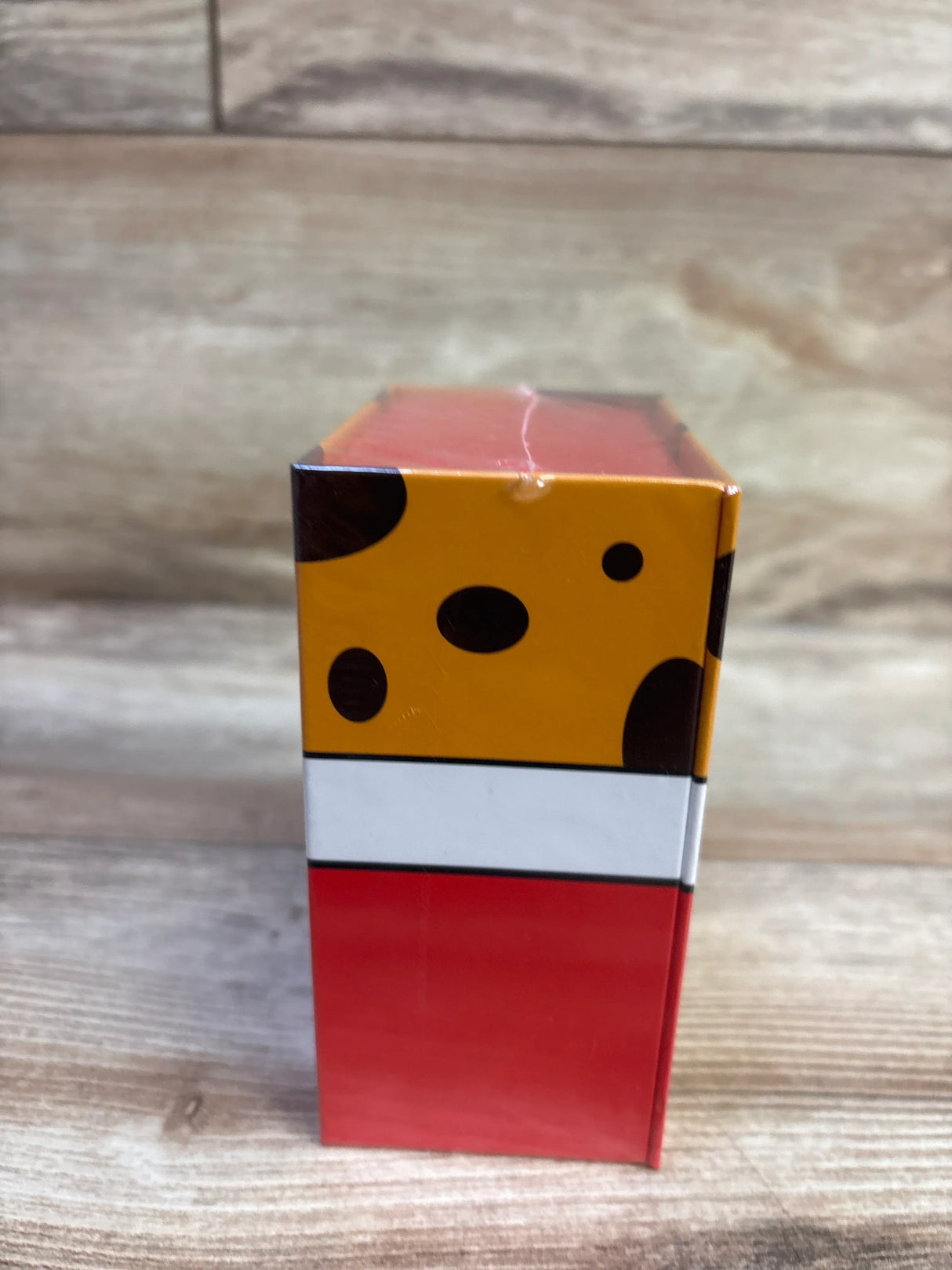 Side view of NEW Chicken or Cheetah card game box showing red lower panel, white stripe and yellow top with brown spots on wood backdrop
