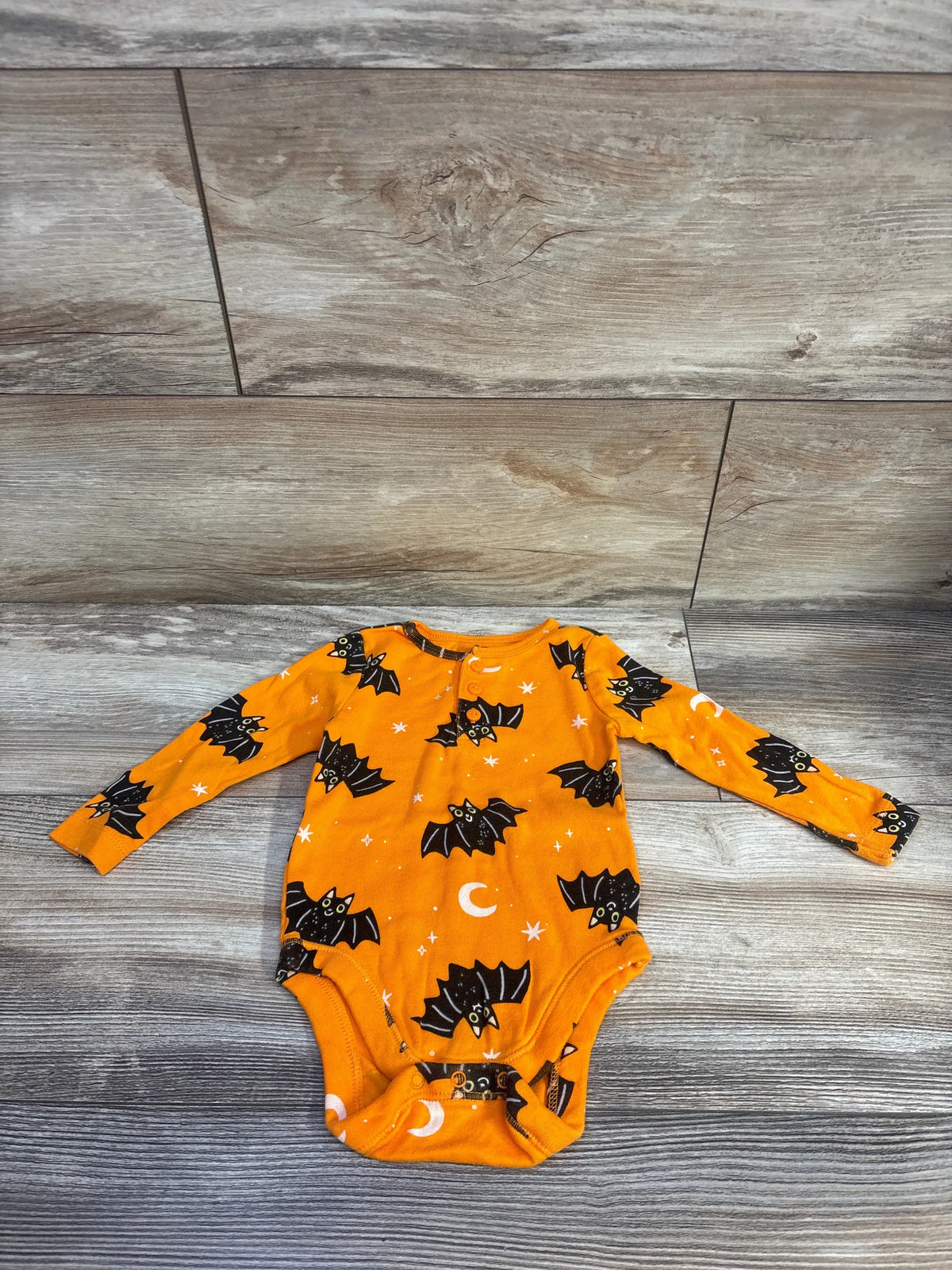 Front view of orange long-sleeve Henley baby bodysuit showcasing black bat and moon print laid flat on wood floor