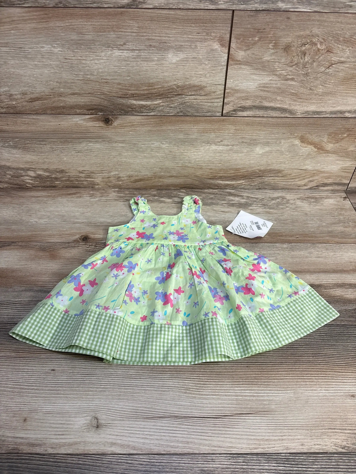 Front view of baby Blueberi Boulevard floral dress, size 3-6 months, light green with pink and purple flowers and green gingham ruffle hem on wood plank background