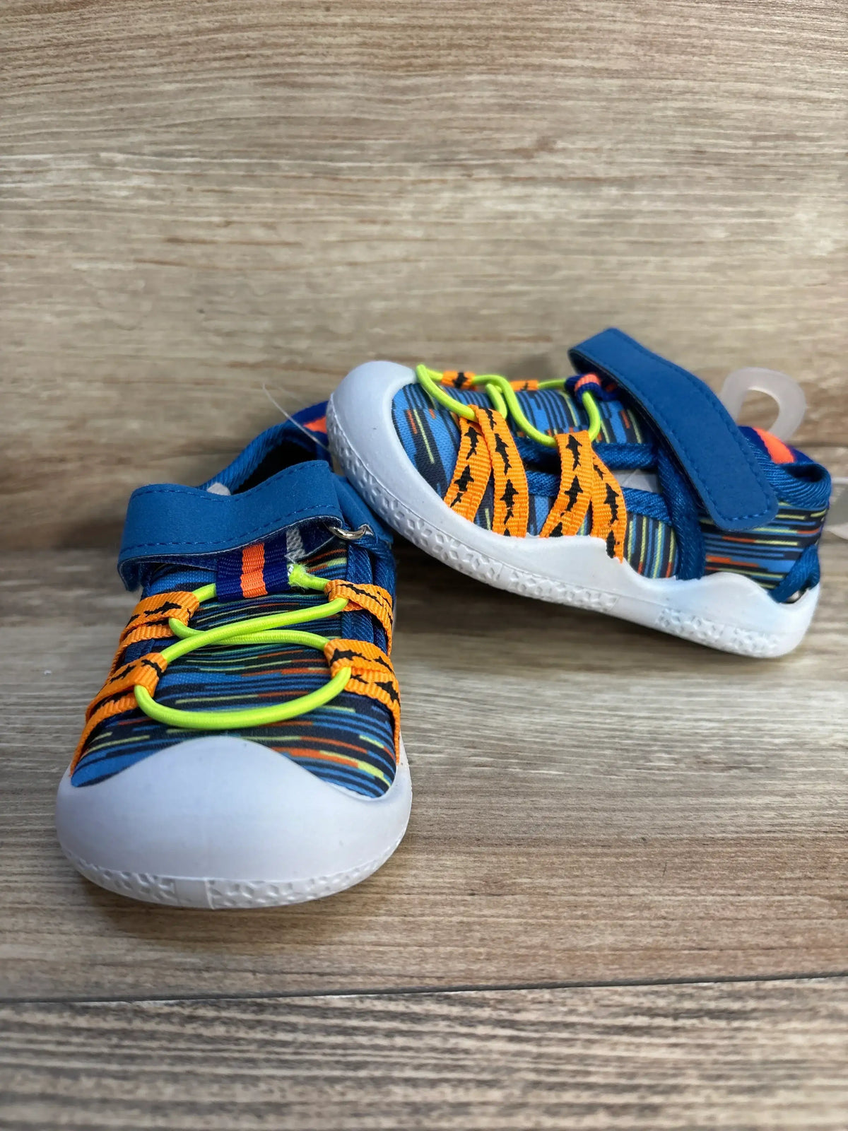 Three-quarter view of toddler Robeez water shoe with blue space-dye mesh, orange straps and neon yellow bungee laces on wood floor