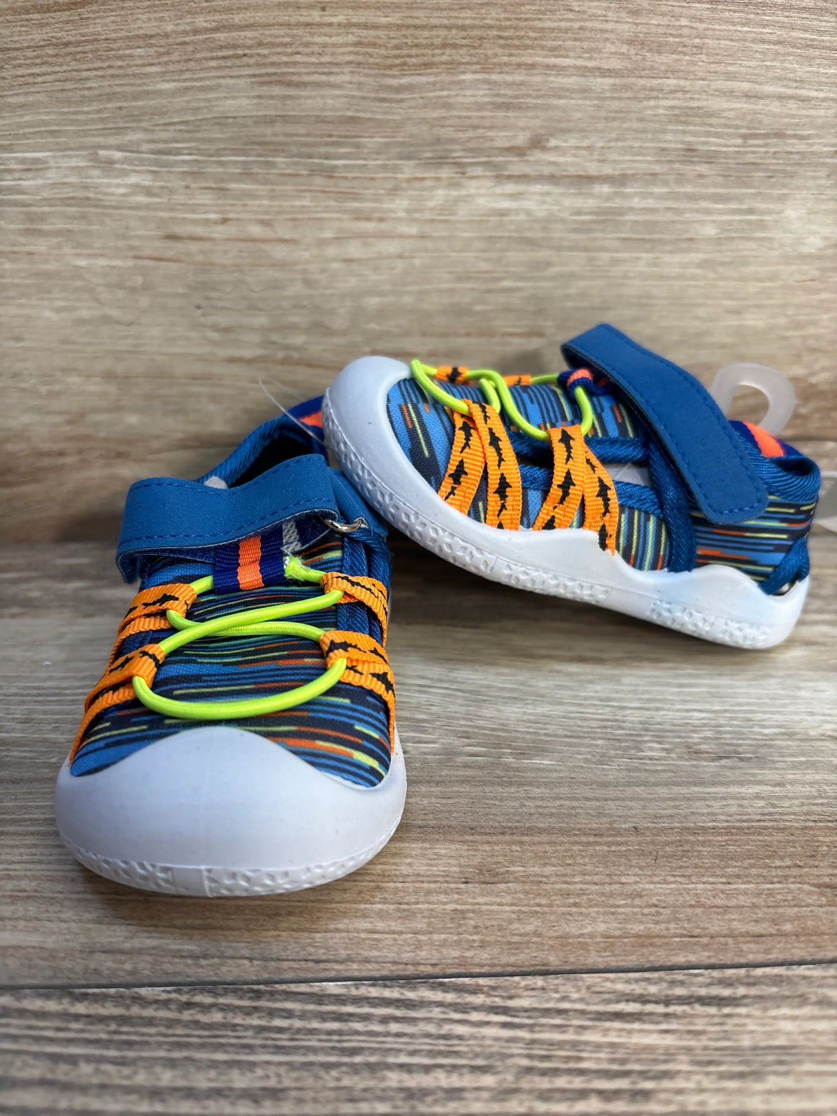 Three-quarter view of Robeez Gradient Mesh Water Shoes Space Dye Sharks showcasing blue striped mesh upper with neon yellow bungee laces on wood plank floor