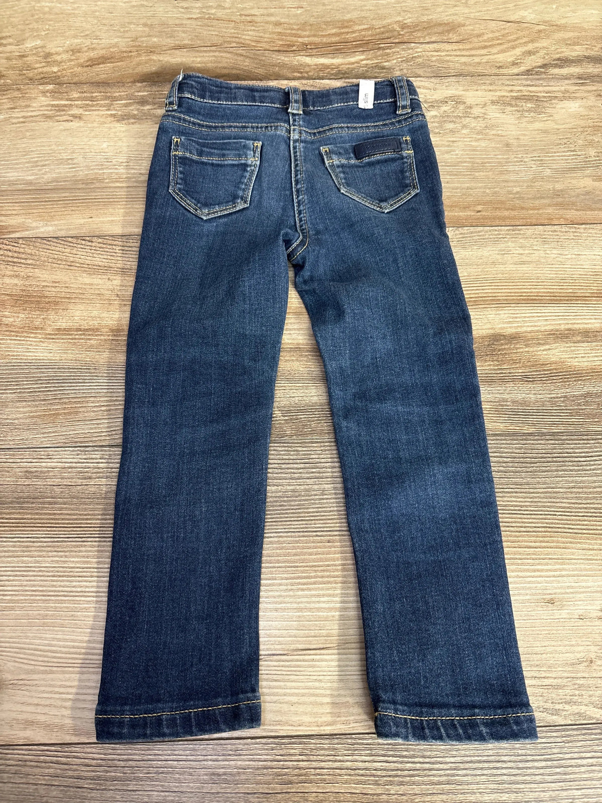 Kids dark wash denim jeans with back pockets displayed on wooden surface