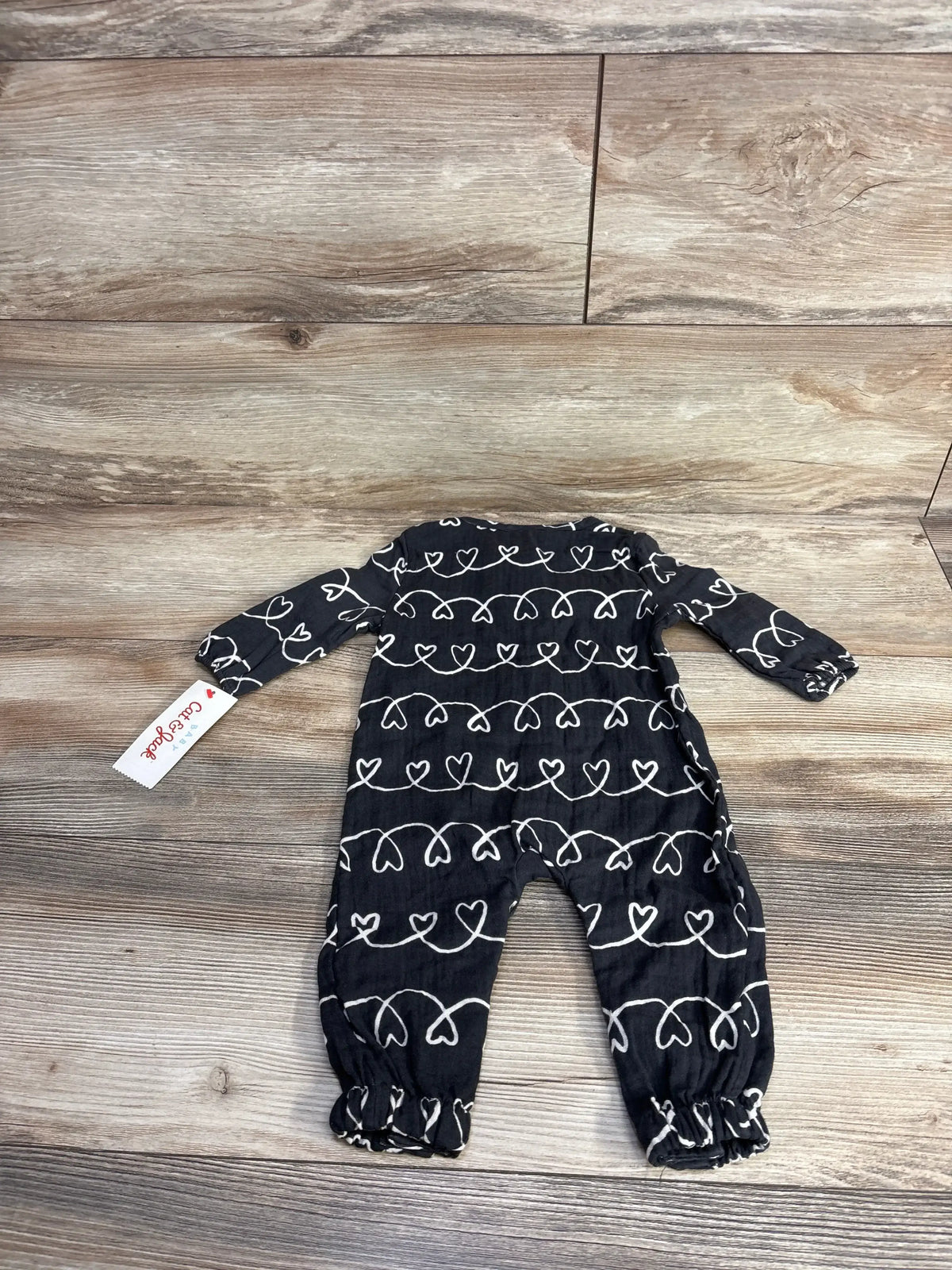Back view flat lay of Cat and Jack jumpsuit in black with white heart print and hangtag on wood plank floor