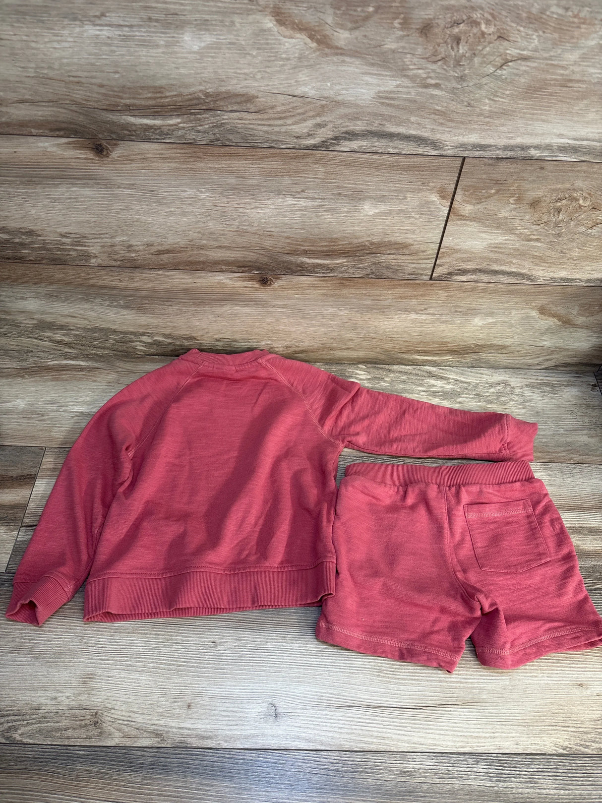Flat lay of Janie & Jack French Terry 2pc Sweatshirt & Shorts Set Red sz 5T showcasing coral crewneck and matching shorts on wood plank floor