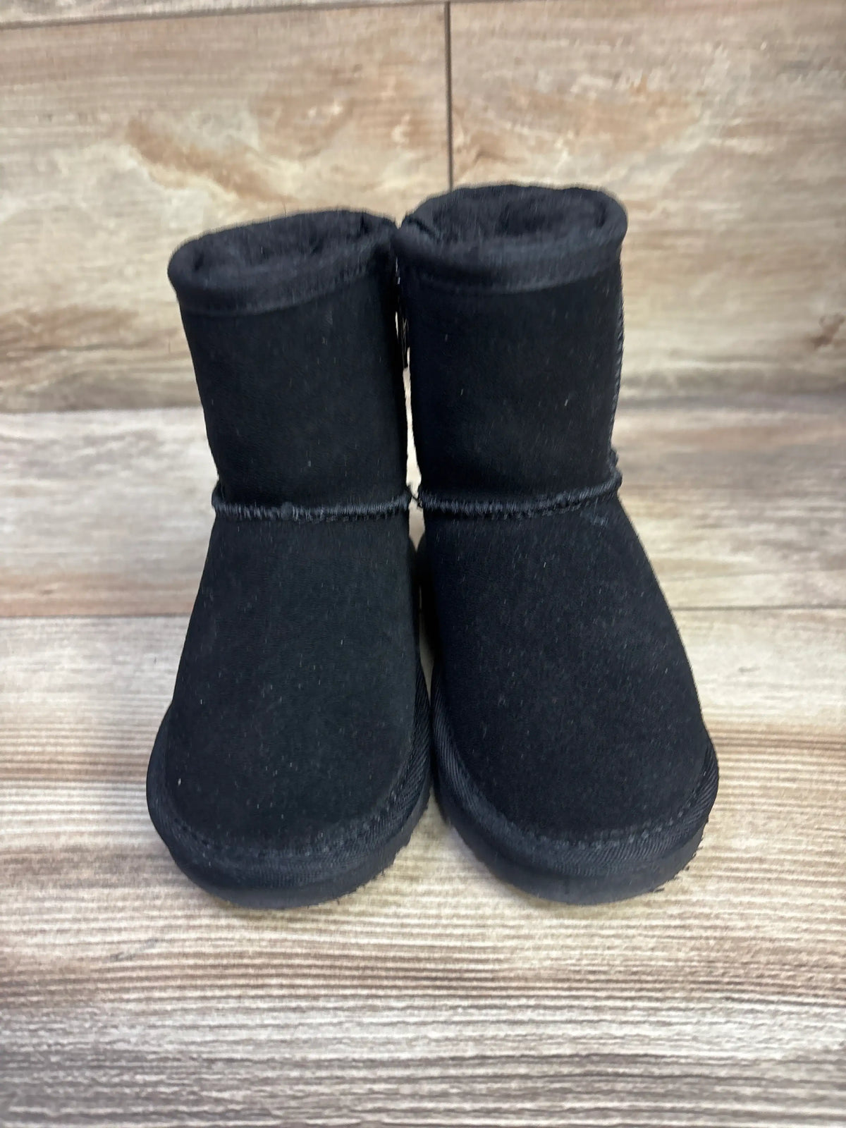 Front view of Bearpaw Emma boots showcasing black ankle-high boots with rounded toes on a wood-grain surface