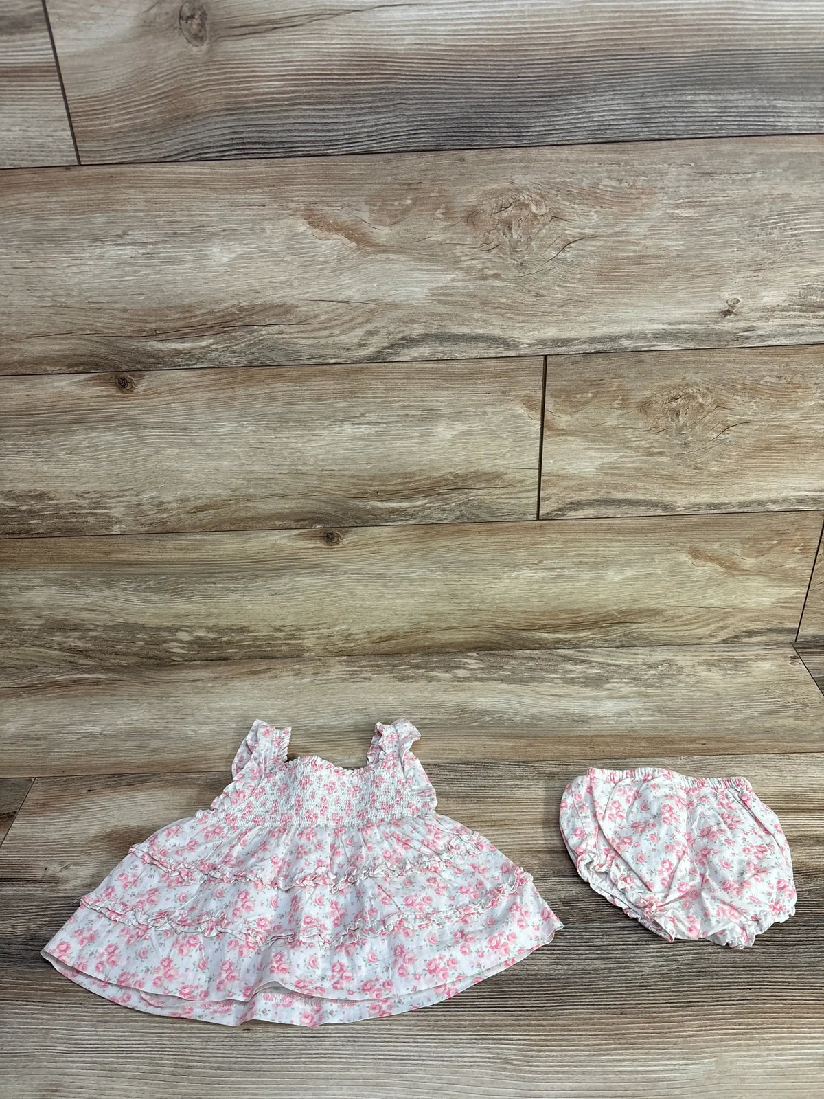 Flat lay of Janie & Jack floral smocked baby dress with matching bloomers, pink floral print on white, wood floor background