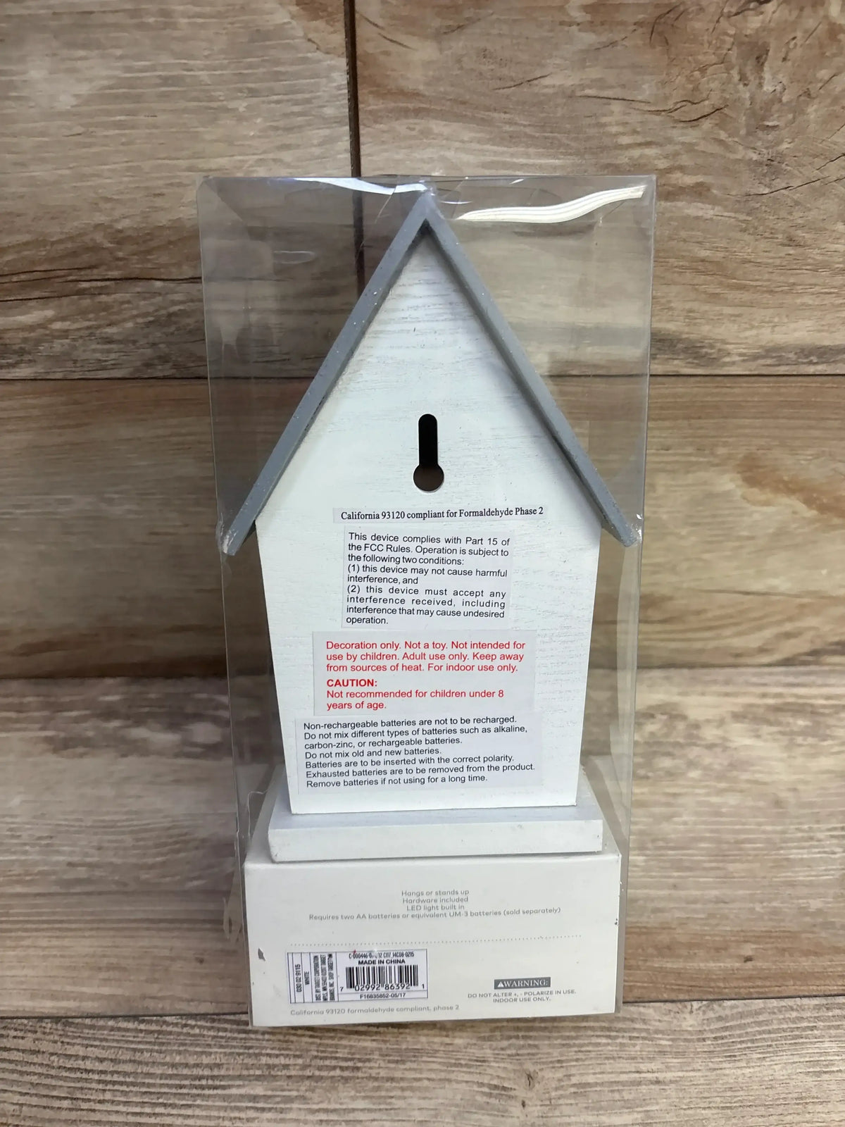 Back view of Cloud Island LED bird house night light showcasing keyhole hanger and warning labels in clear plastic box on wood background