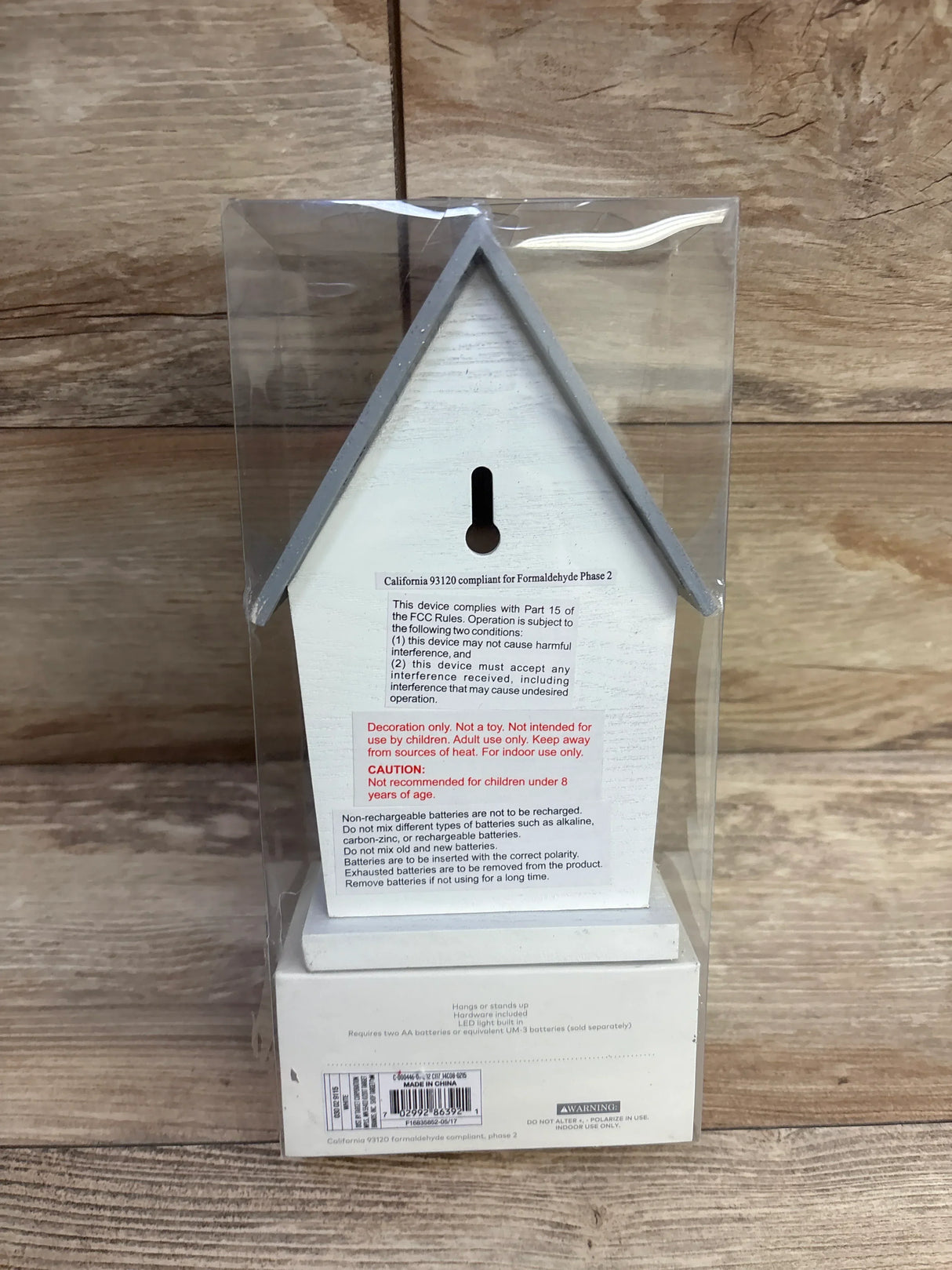 Back view of Cloud Island LED bird house night light showcasing keyhole hanger and warning labels in clear plastic box on wood background