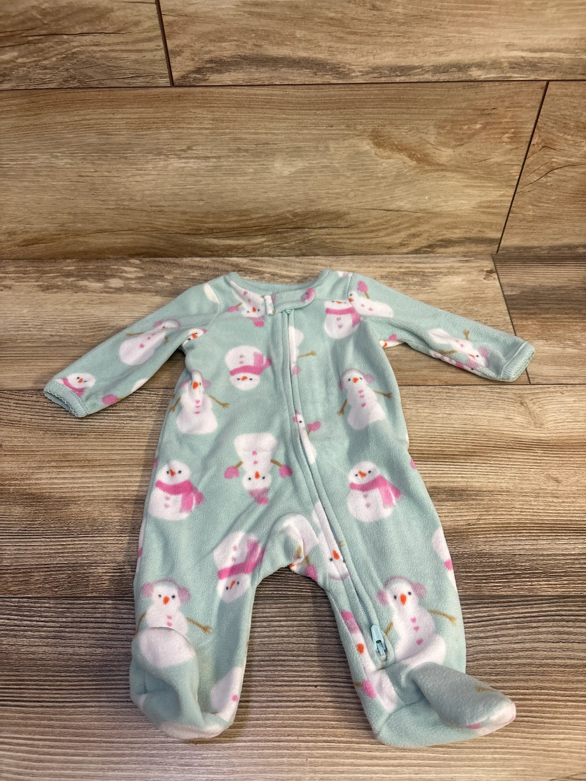 Front view of blue newborn blanket sleeper showcasing snowman print, long sleeves, footed legs, and full-length zipper on wood flooring