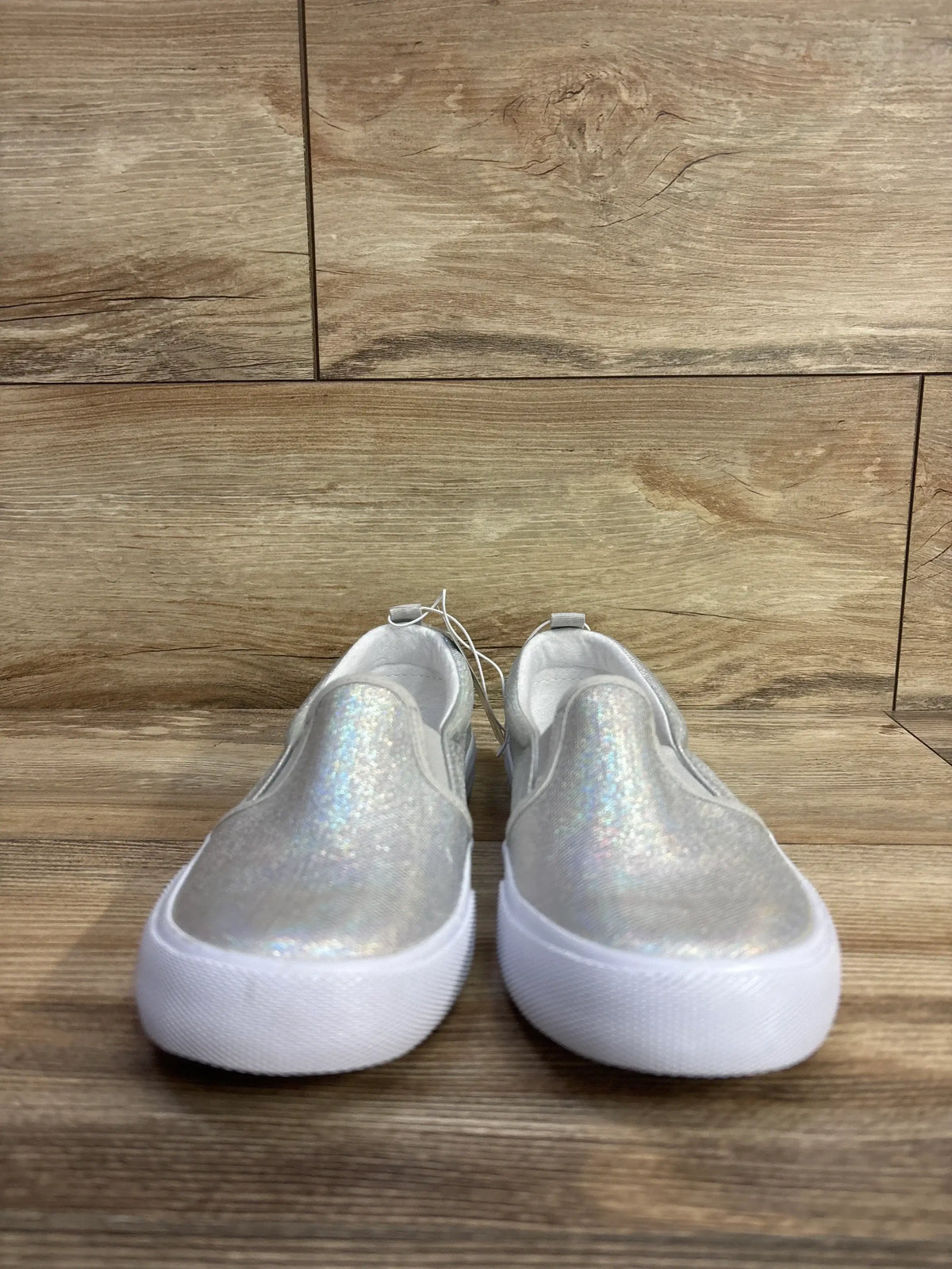 Pair of iridescent silver slip-on kids shoes with white soles on wooden floor
