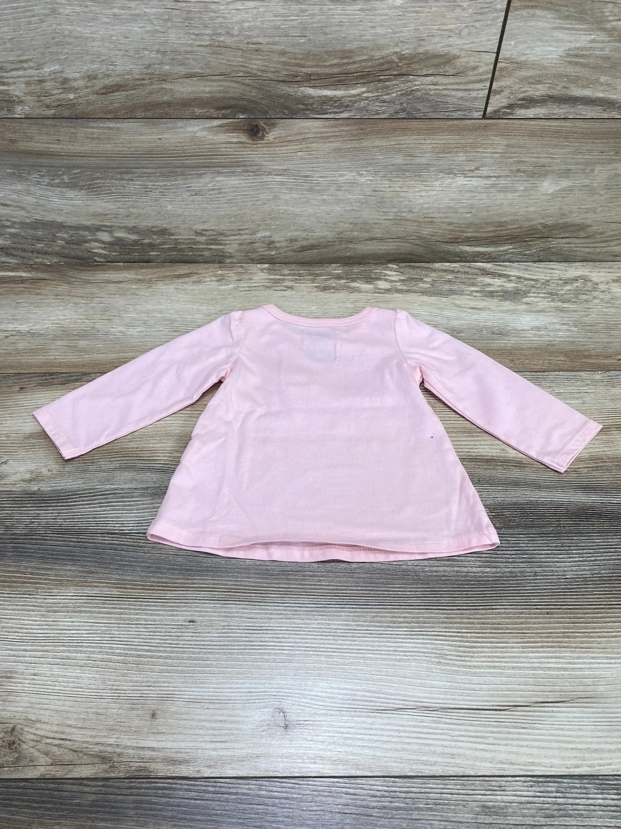 Back view flat lay of First Impressions pink long-sleeve baby shirt 6 to 9 months showing A-line swing hem on wood plank background