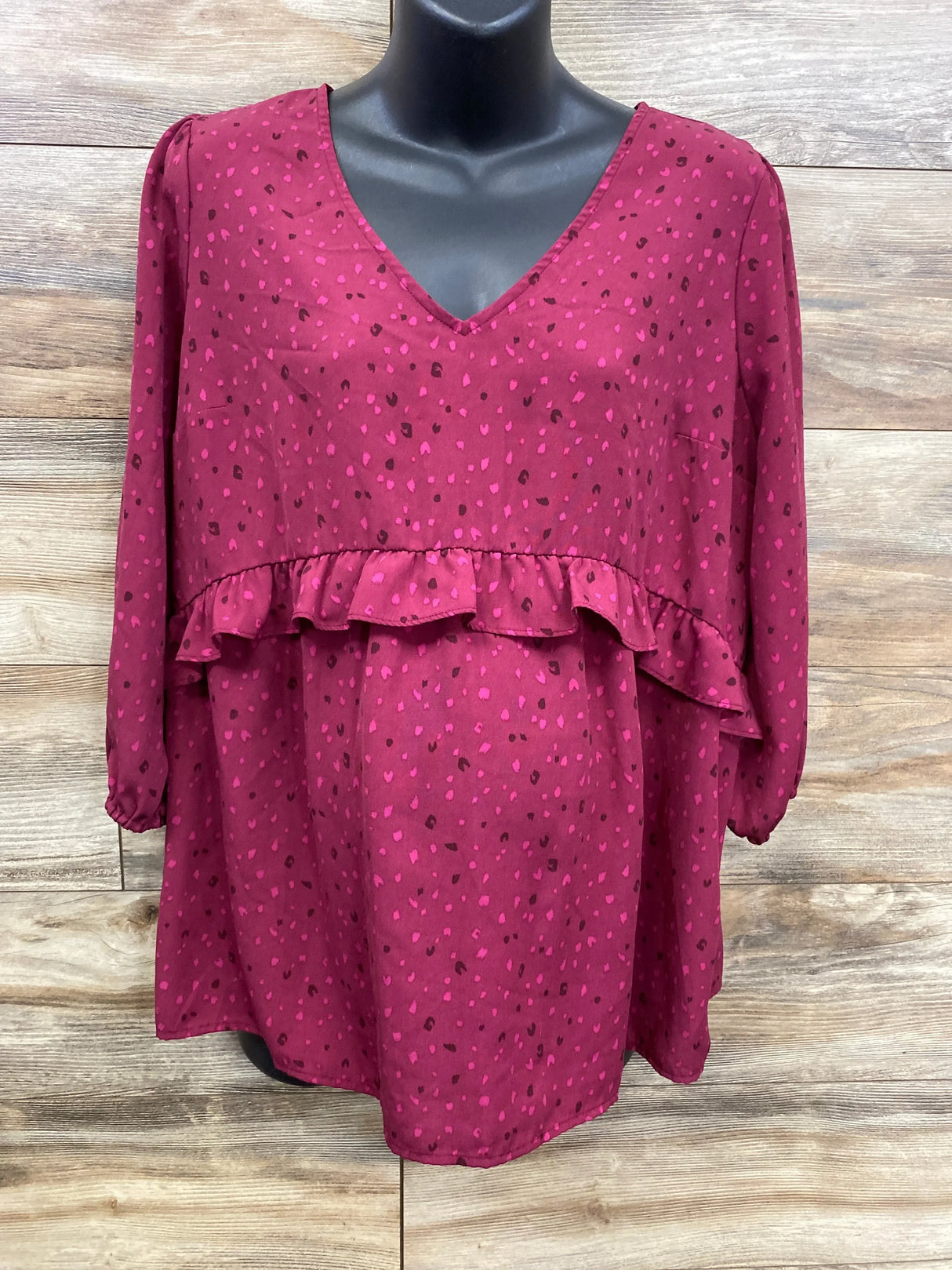 Burgundy maternity blouse with pink polka dots, ruffle detail, and V-neck on mannequin