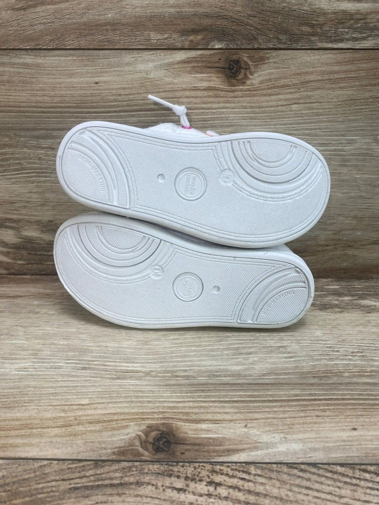 Bottom view of Wonder Nation girls' casual bump-toe sneakers showing clean white non-marking soles on wood background