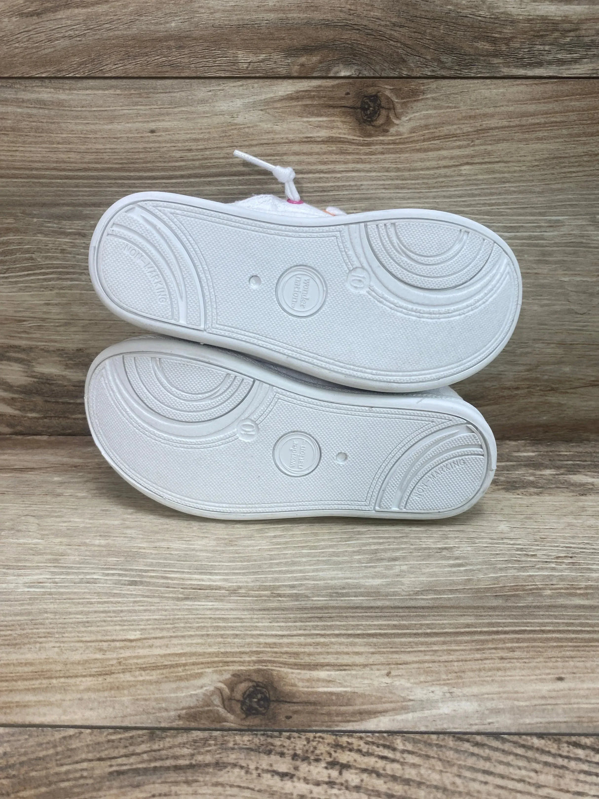 Bottom view of Wonder Nation girls' casual bump-toe sneakers showing clean white non-marking soles on wood background