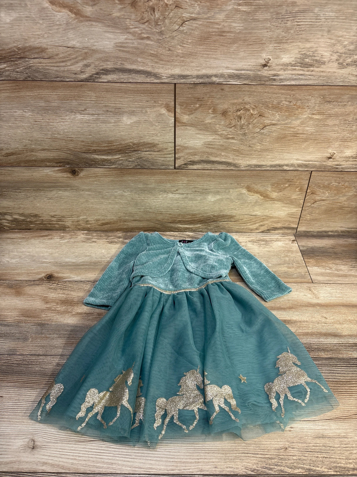 Flat lay of green velvet cardigan and tulle dress set with glitter unicorn hem on wood background