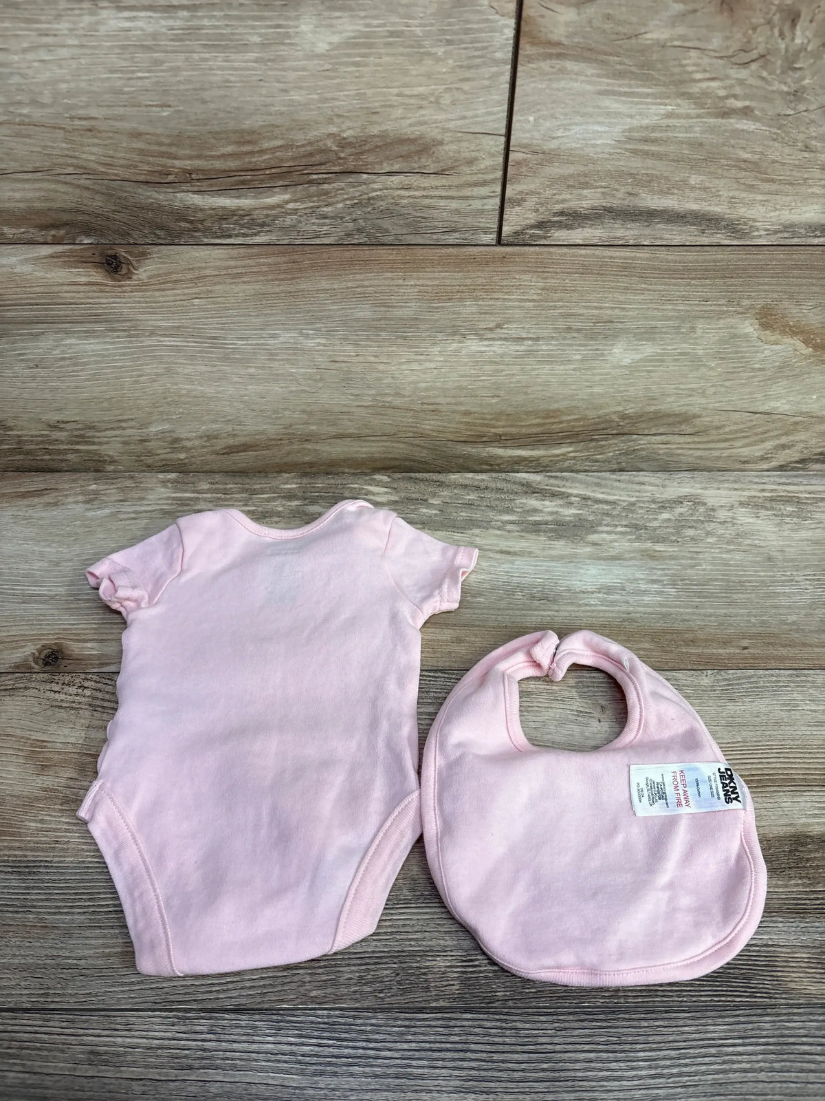 Light pink baby bodysuit and matching bib on wooden floor background