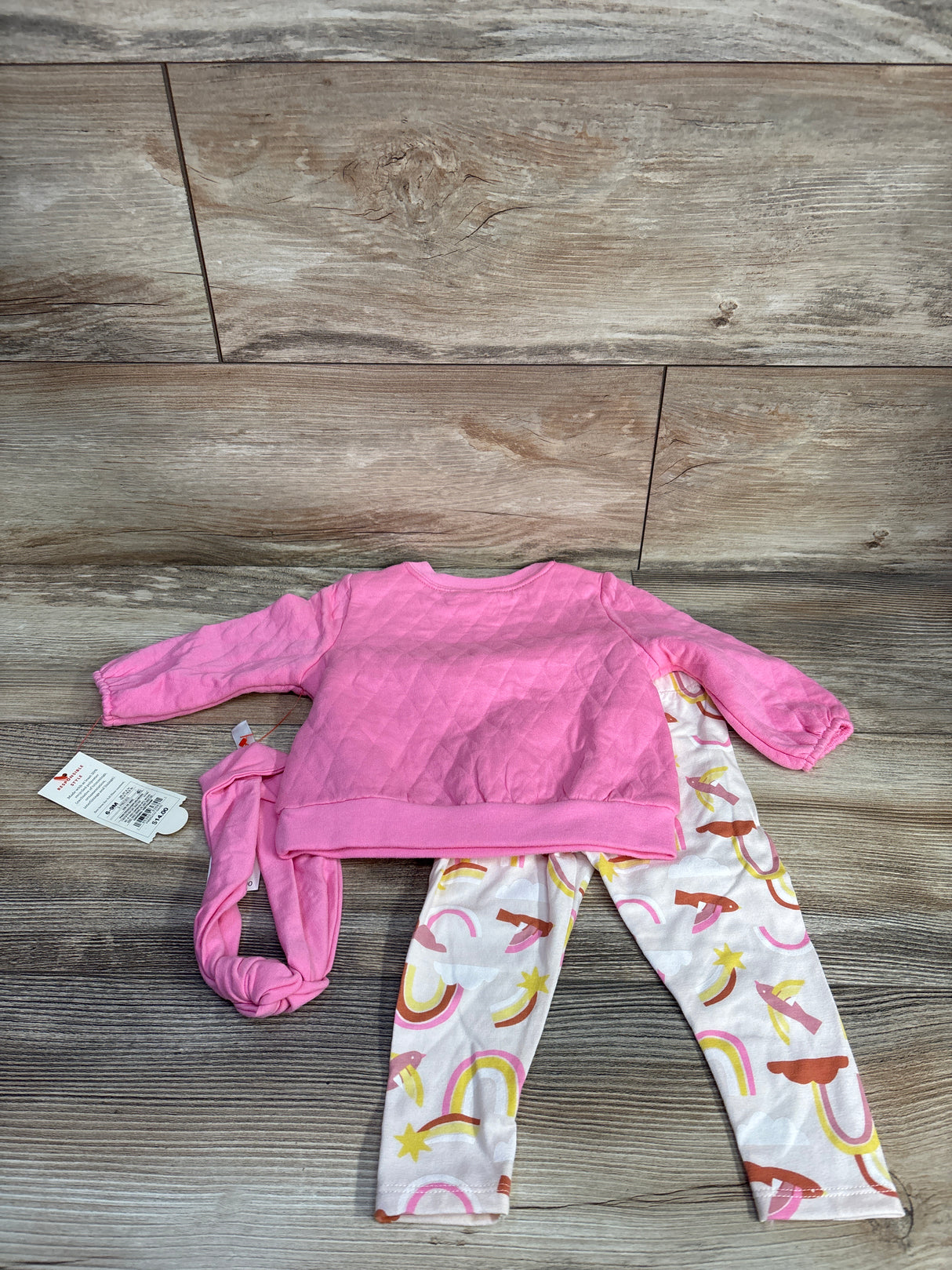 Pink quilted baby sweatshirt with matching headband and multicolor rainbow and star patterned leggings on wood floor