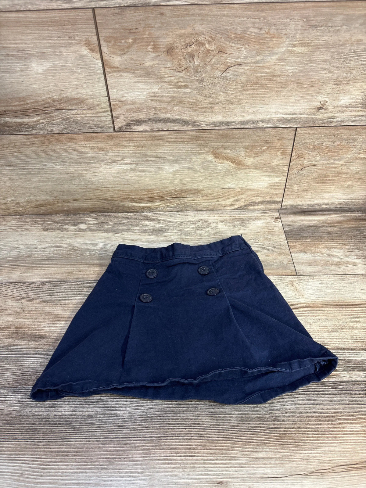 Flat lay of navy Children’s Place ponte knit skort (size 5T) showcasing double front buttons and box pleats on a wood floor background