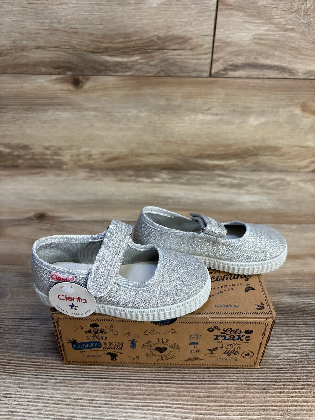 Silver glitter toddler Mary Jane shoes with velcro strap on branded box, wood background