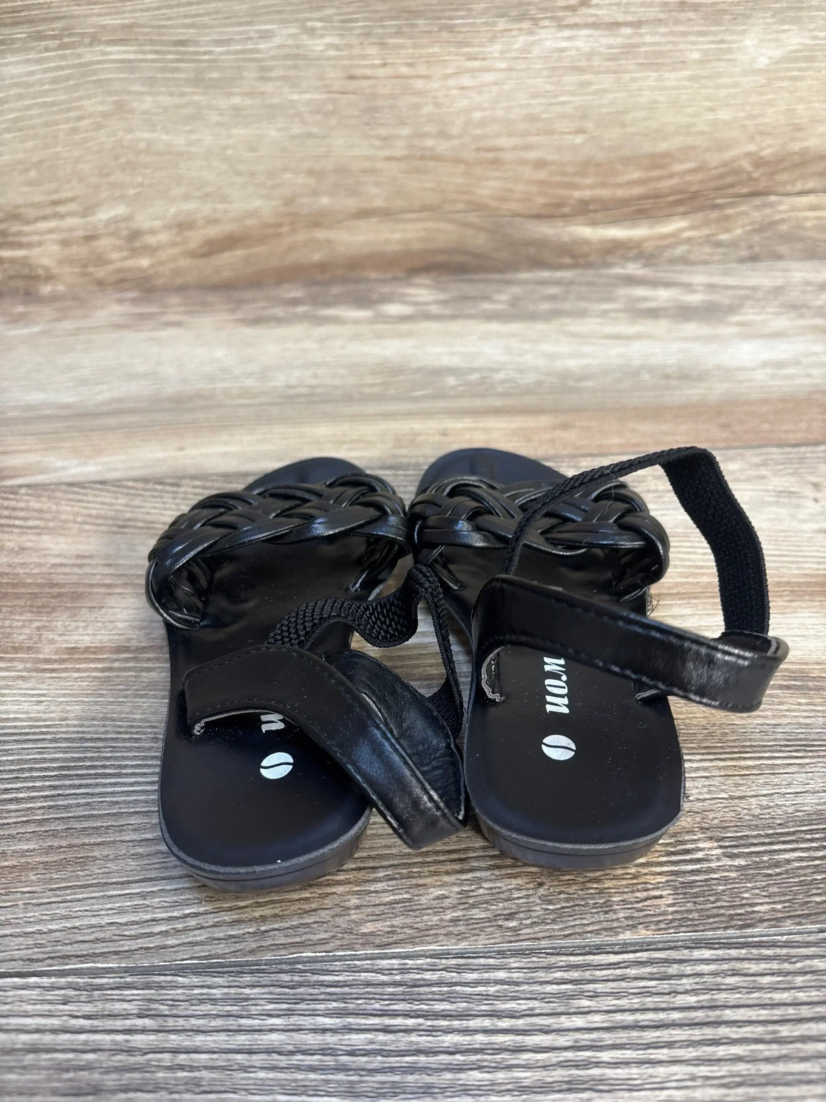 Front view of black WON braided toddler sandals showcasing braided upper and Velcro ankle straps on a wood floor