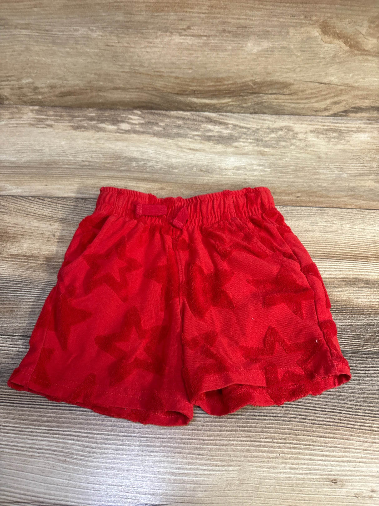 Front view of red terry cloth star shorts with embossed stars and elastic waistband on wood background