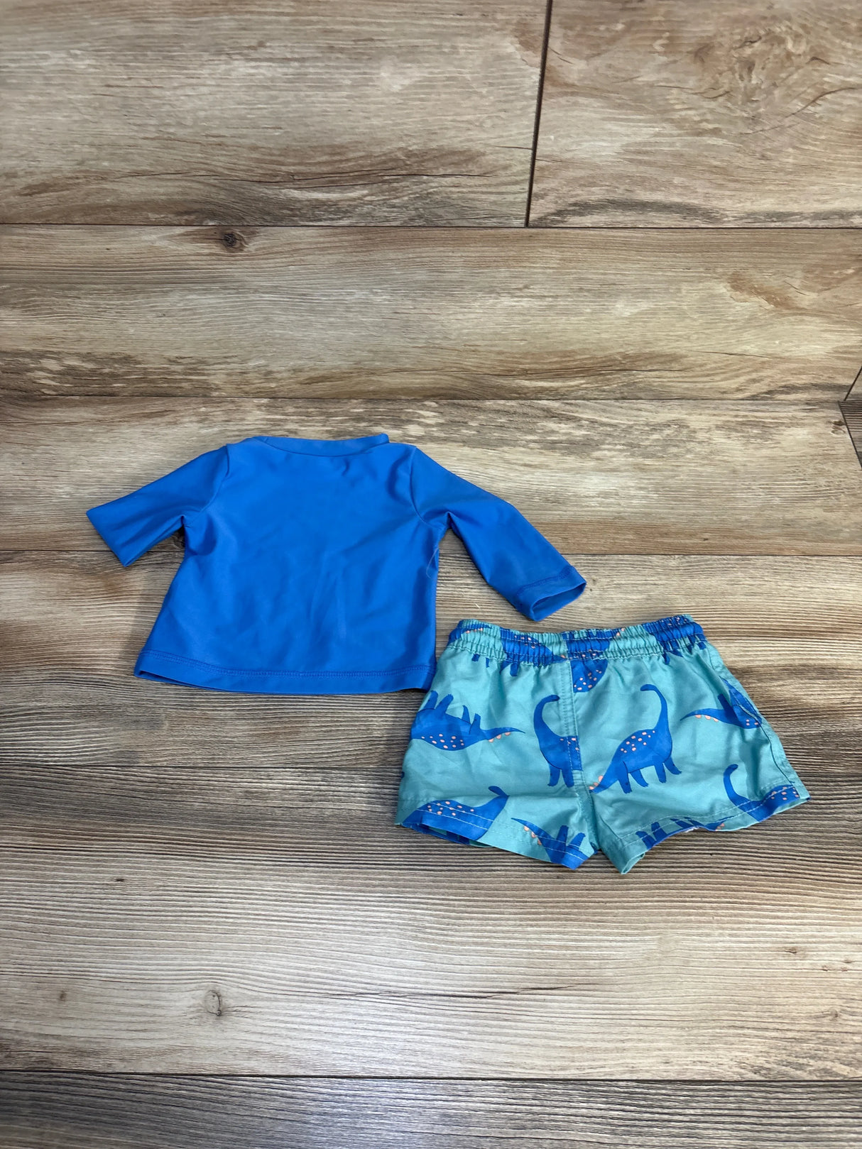 Blue toddler swim set with dinosaur print shorts and long-sleeve rash guard on wood floor
